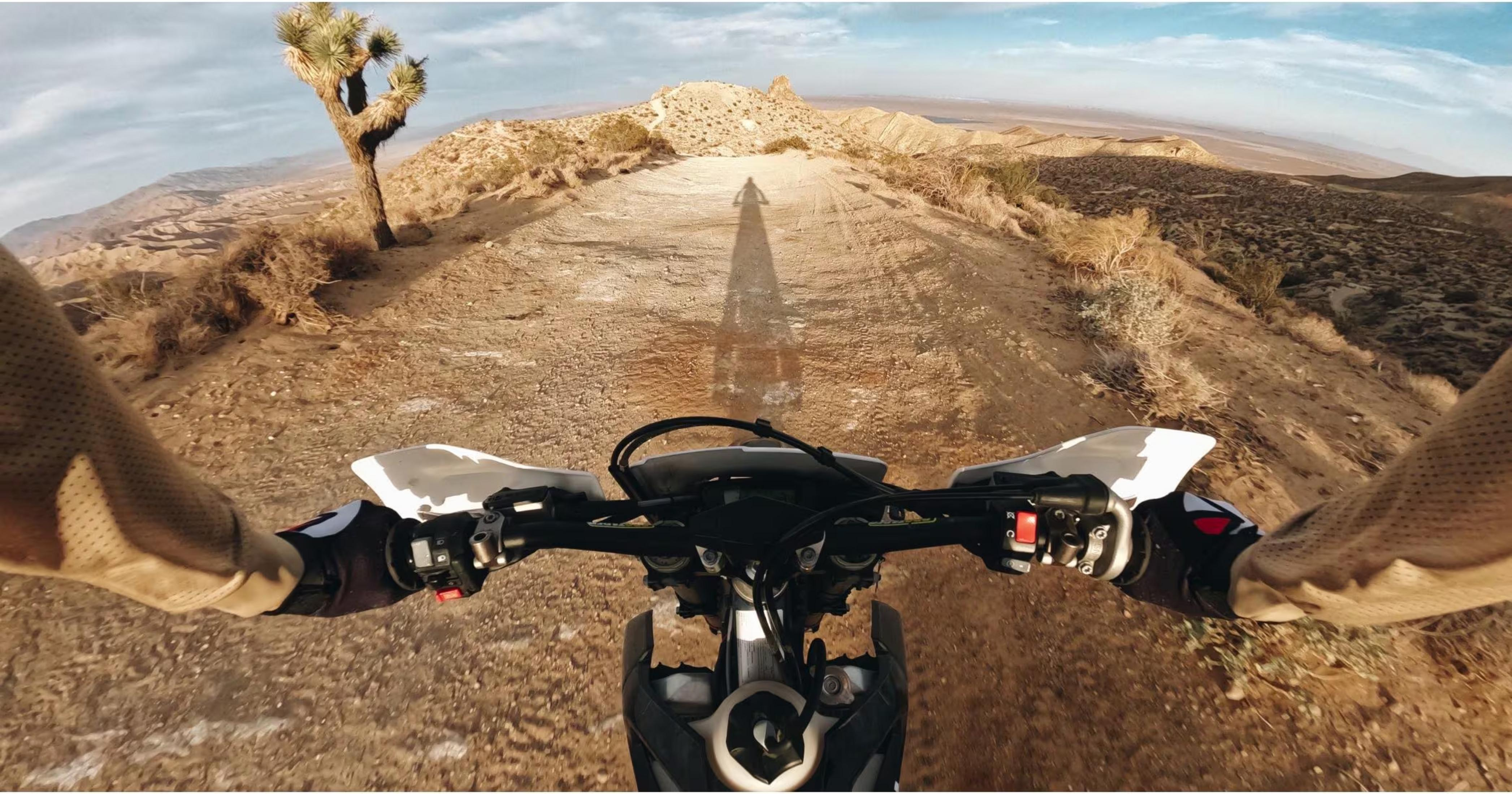 Widok z pierwszej osoby na motocykl, jadący polną drogą na pustyni.