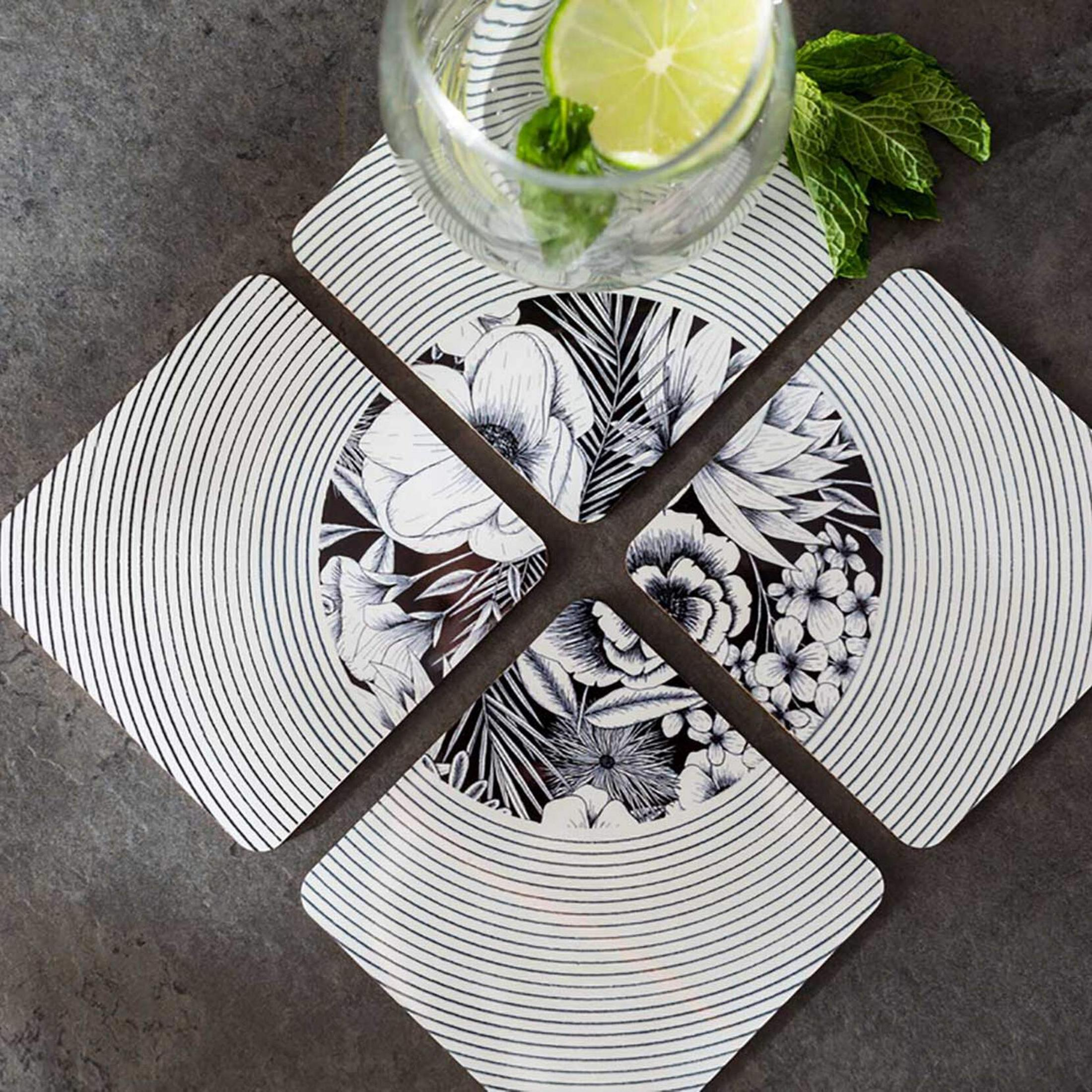 Quatre sous-verres à motifs floraux et rayés, avec un verre de citron vert et de menthe.