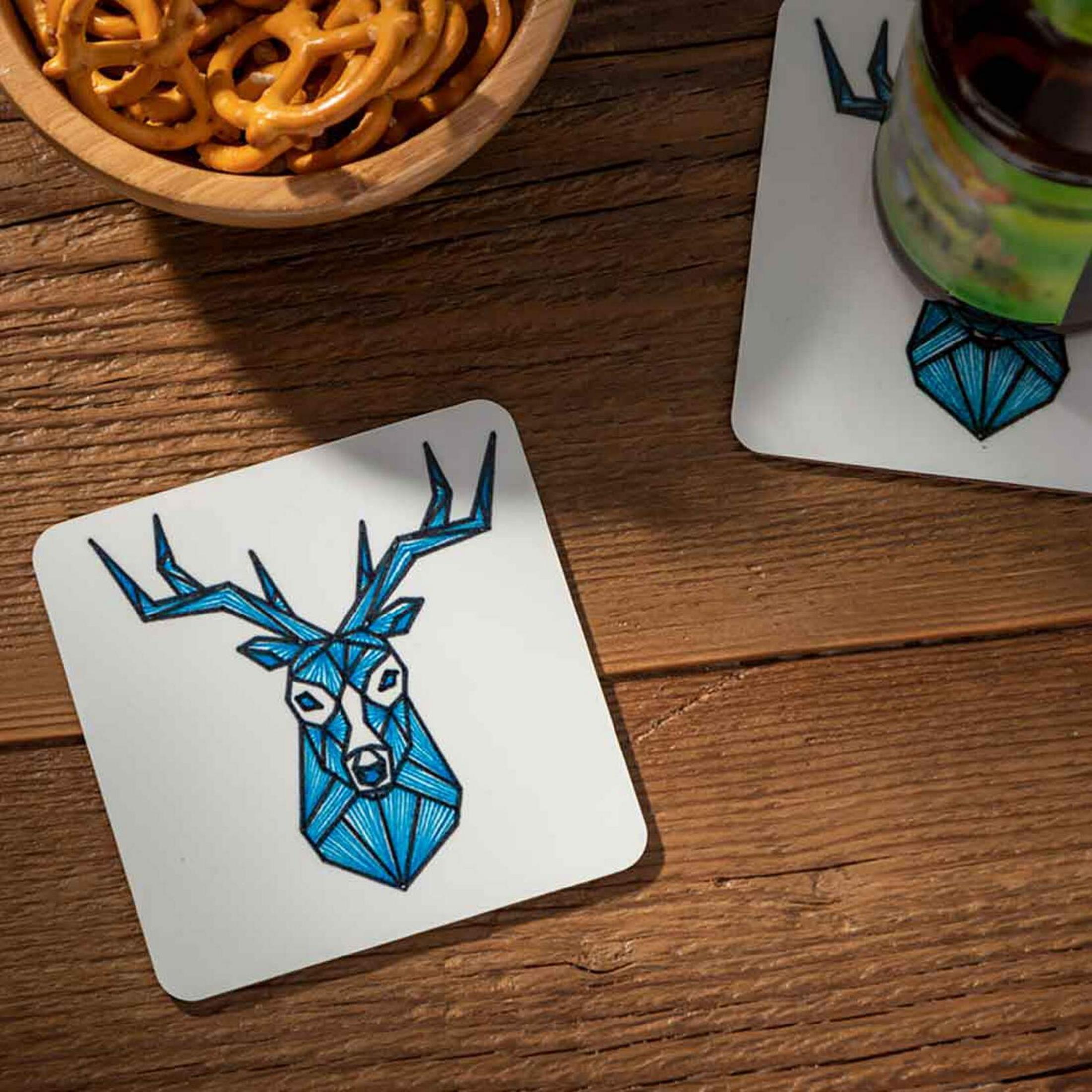 Un sous-verre avec un motif de tête de cerf bleue repose sur une table en bois près d'un bol de bretzels.