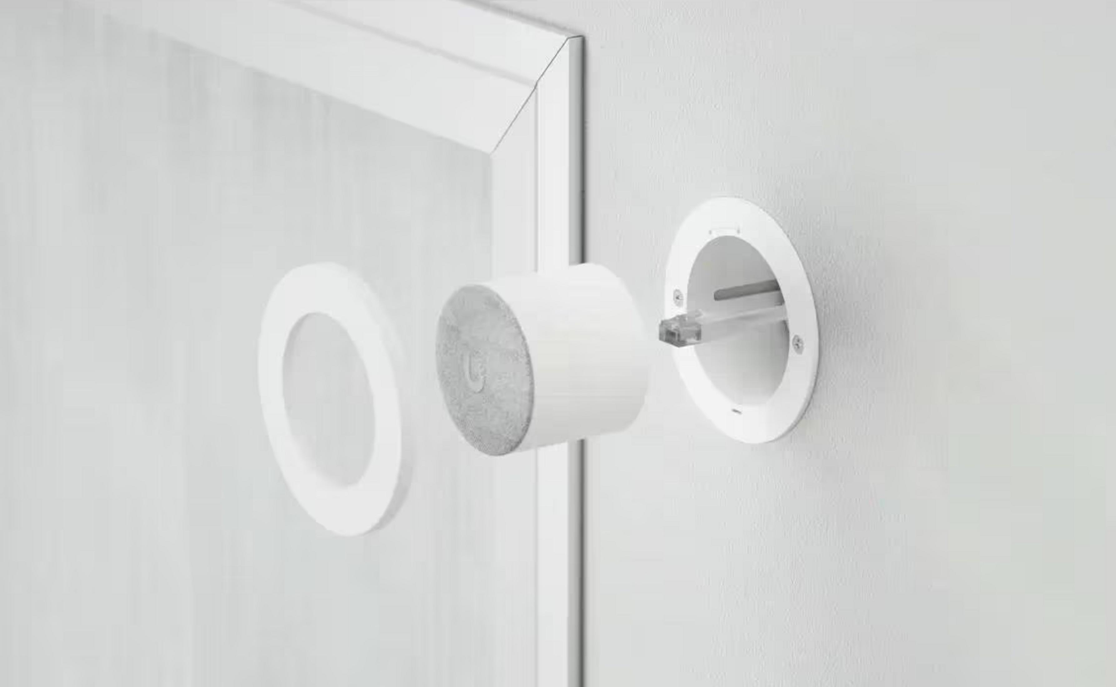 A white speaker is being inserted into a wall mount.