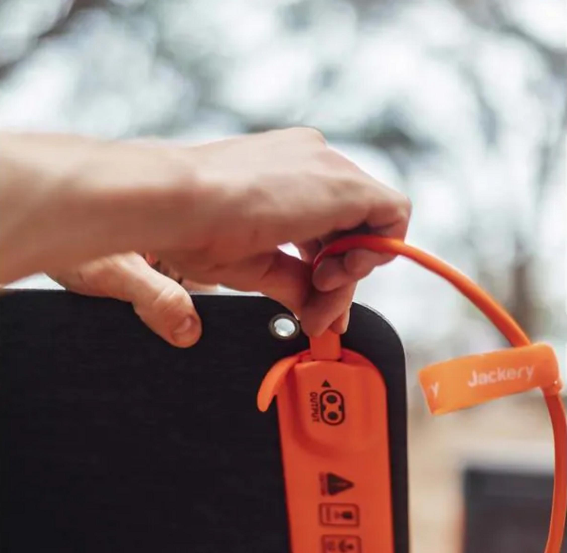 Hand houdt oranje kabel vast aan zwart apparaat met Jackery-logo.