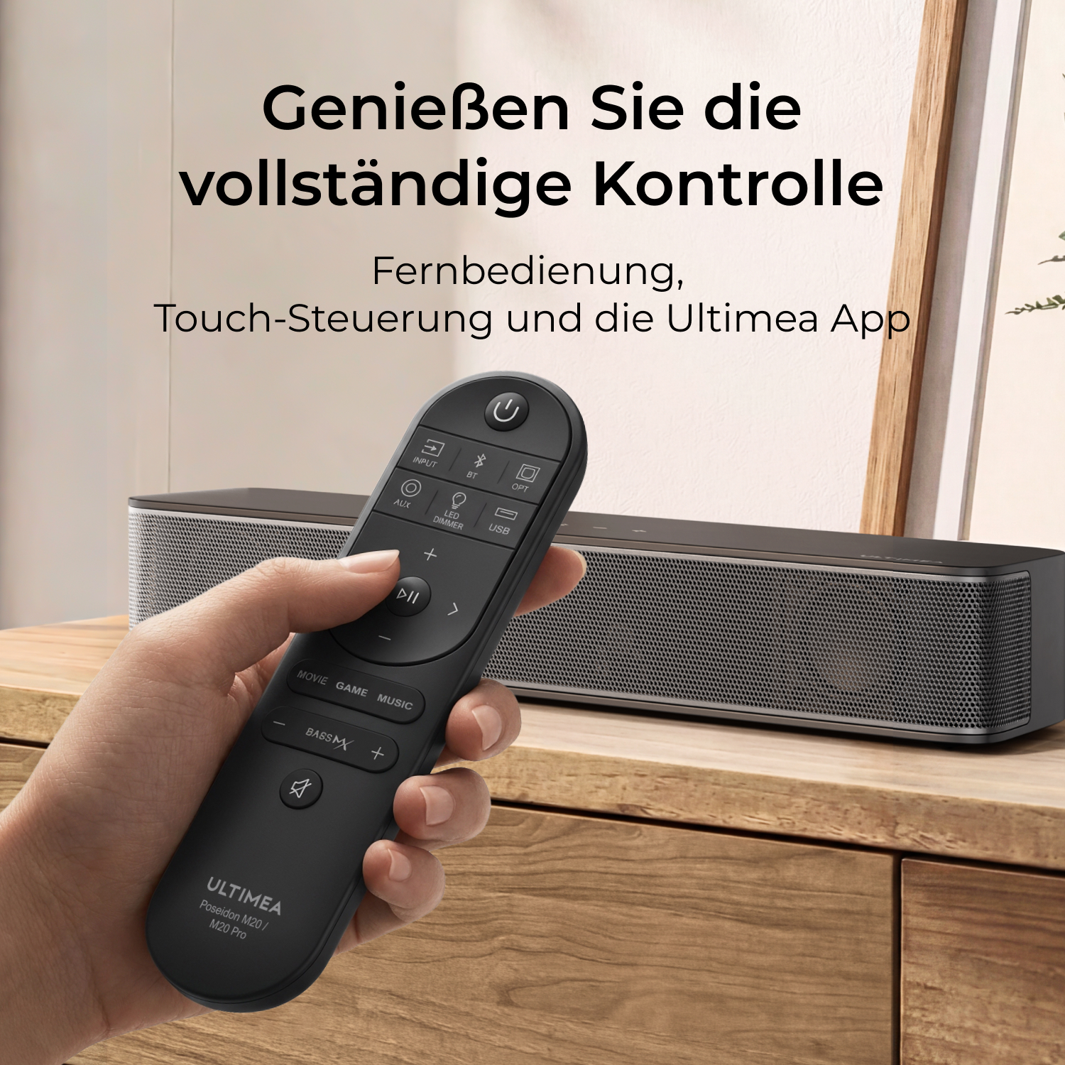Eine Hand hält eine schwarze Fernbedienung für eine Soundbar, die auf einem Holzmöbel steht.