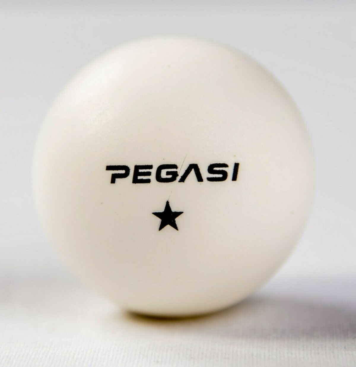 A white table tennis ball with black lettering "PEGASI" and a star.