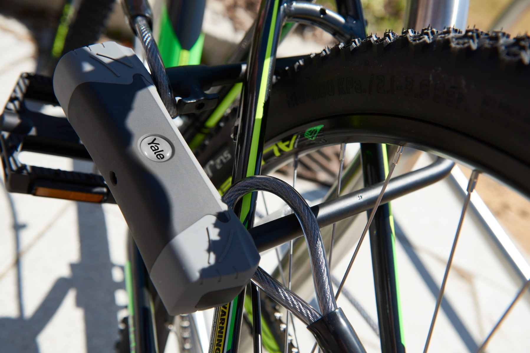 Un candado de bicicleta Yale gris está sujeto al cuadro y rueda de una bicicleta verde y negra.