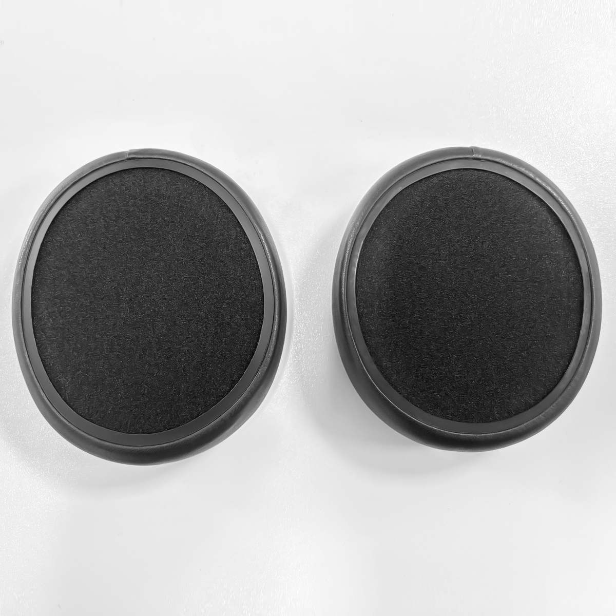 Dwa czarne, okrągłe nauszniki leżą obok siebie na białej powierzchni.