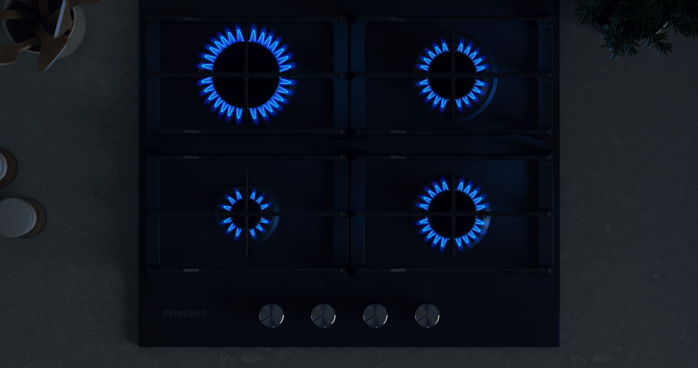 Czarna płyta gazowa z czterema niebieskimi płomieniami w ciemności.