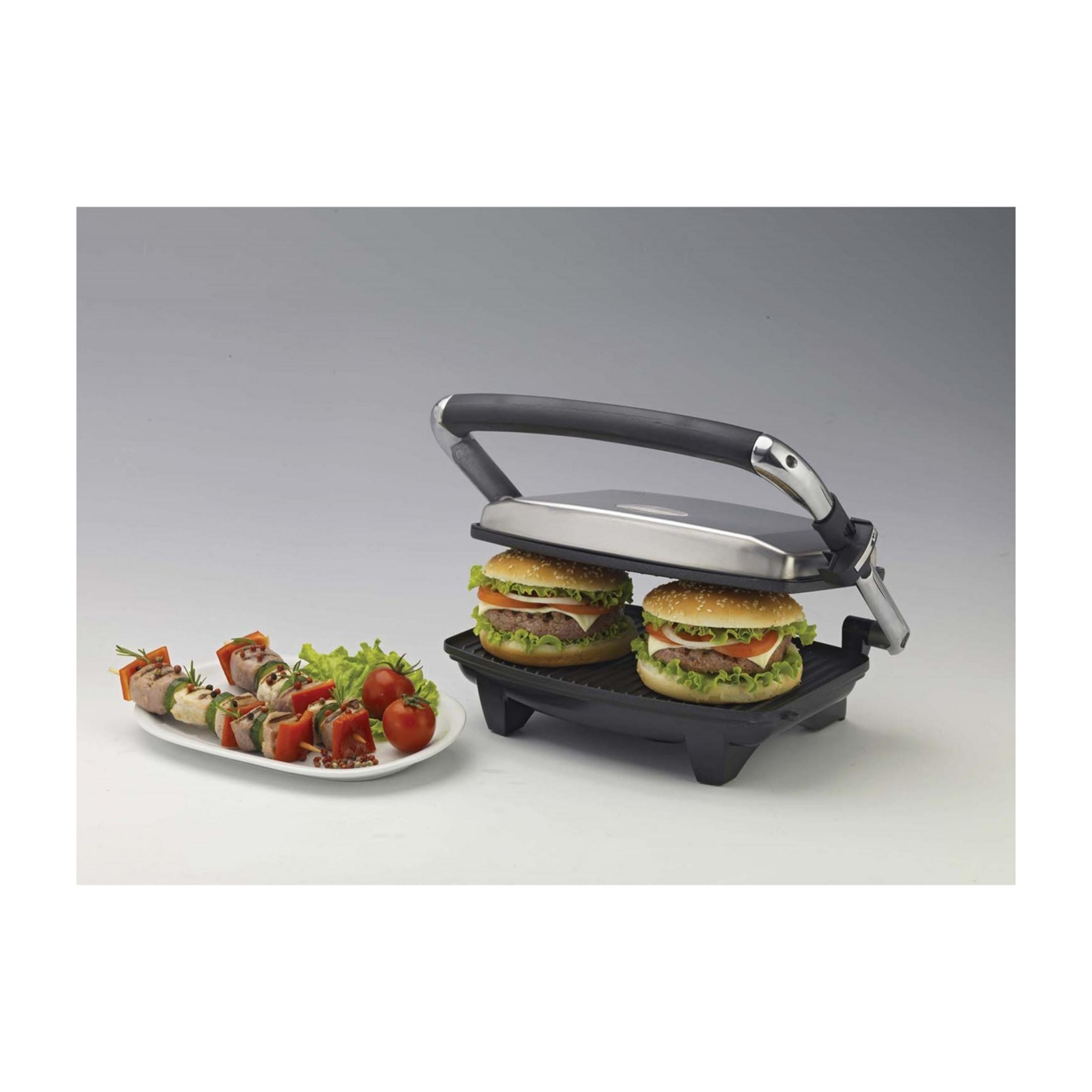 Una plancha para paninis con dos hamburguesas y un plato de brochetas y ensalada.