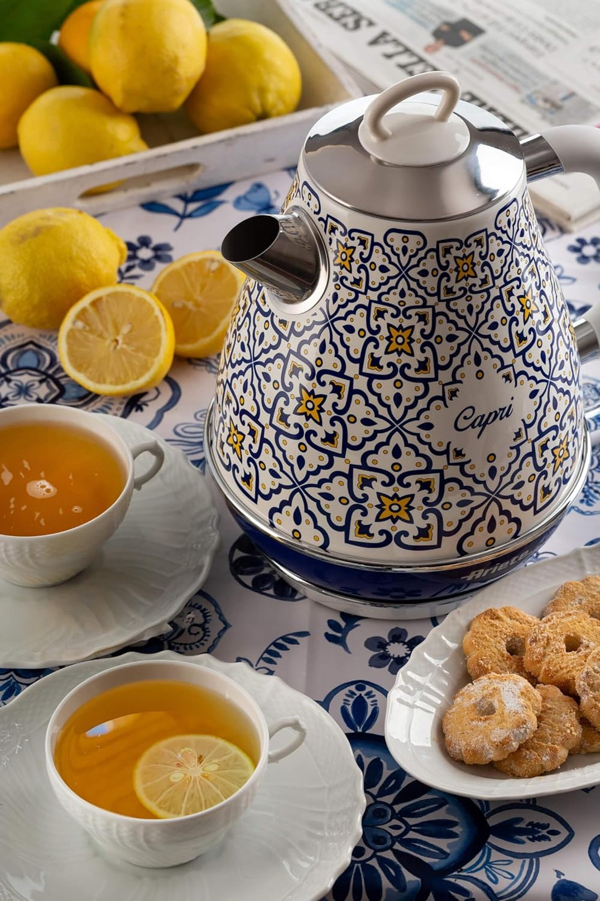 Dekoracyjny czajnik z niebiesko-białymi wzorami, obok cytryn, herbaty i ciastek.