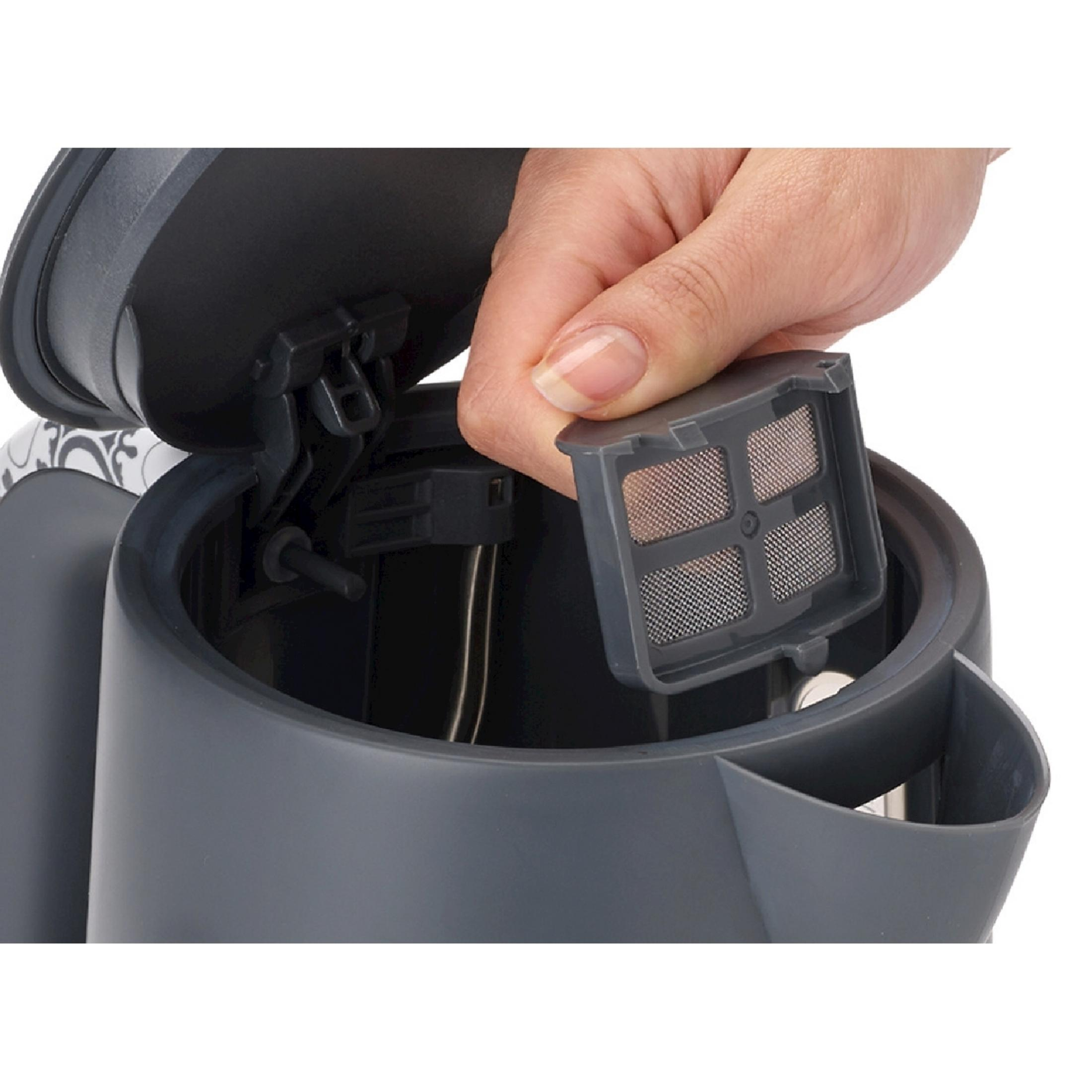 A hand holds a gray mesh tea filter in front of a gray kettle.