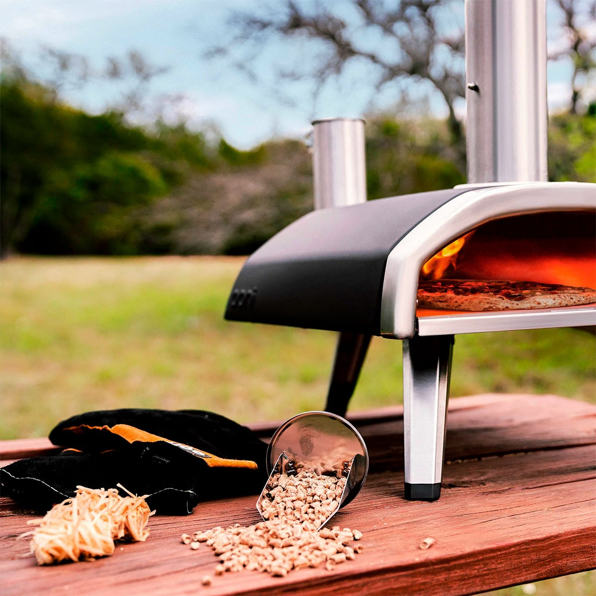 Un forno per pizza con una pizza all'interno, pellet e guanti su un tavolo.