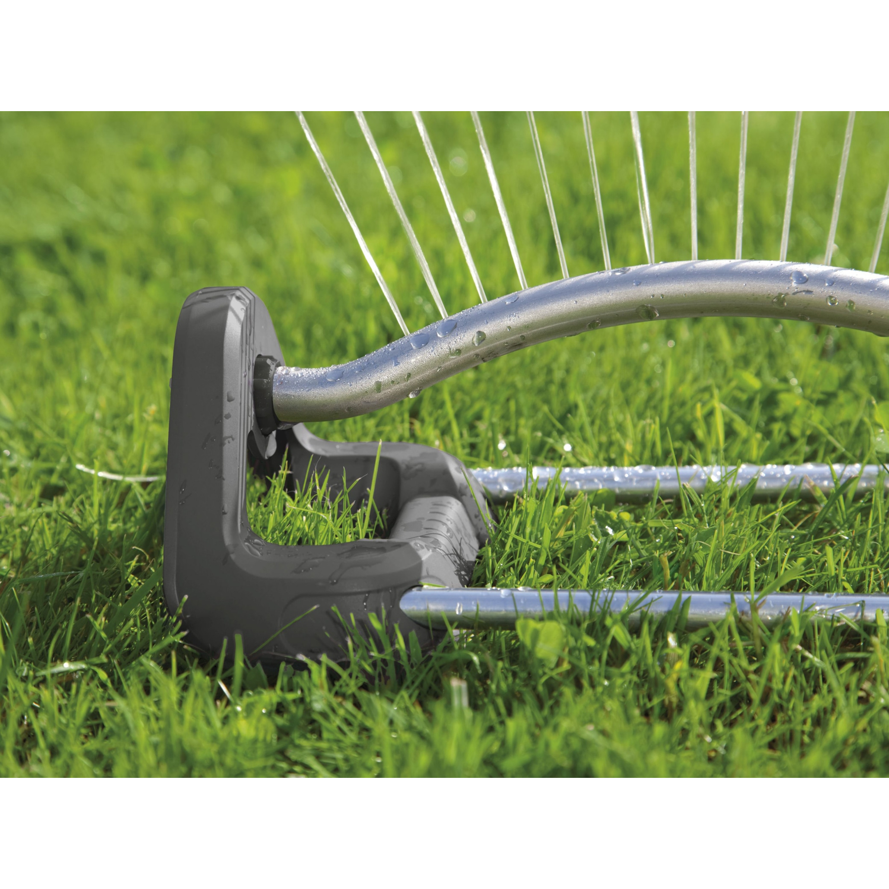Ein Sprinkler mit Metallrohr und dunklem Sockel bewässert grünes Gras.