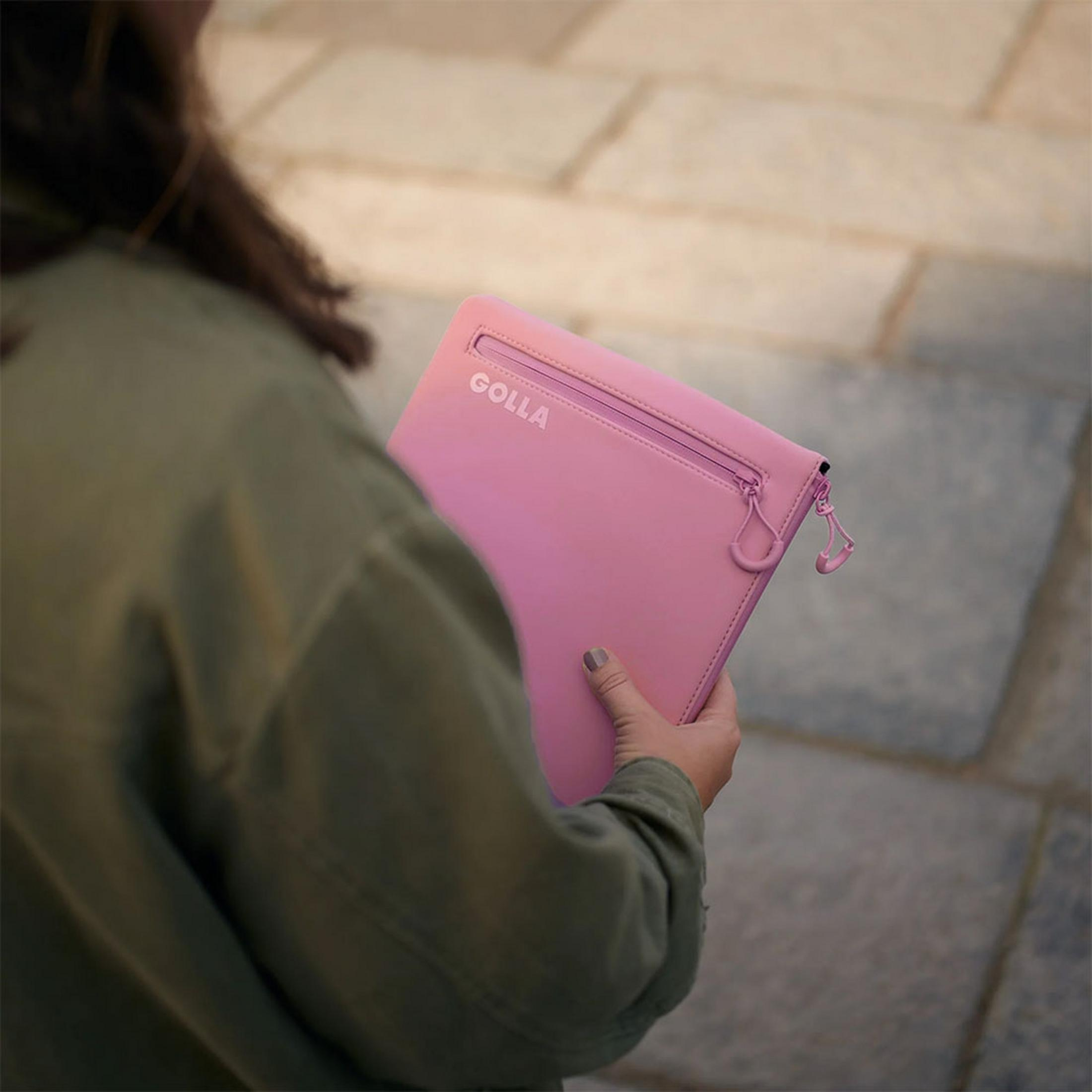 Eine Person hält eine pinke Golla Tasche in der Hand, draußen auf einem Gehweg.