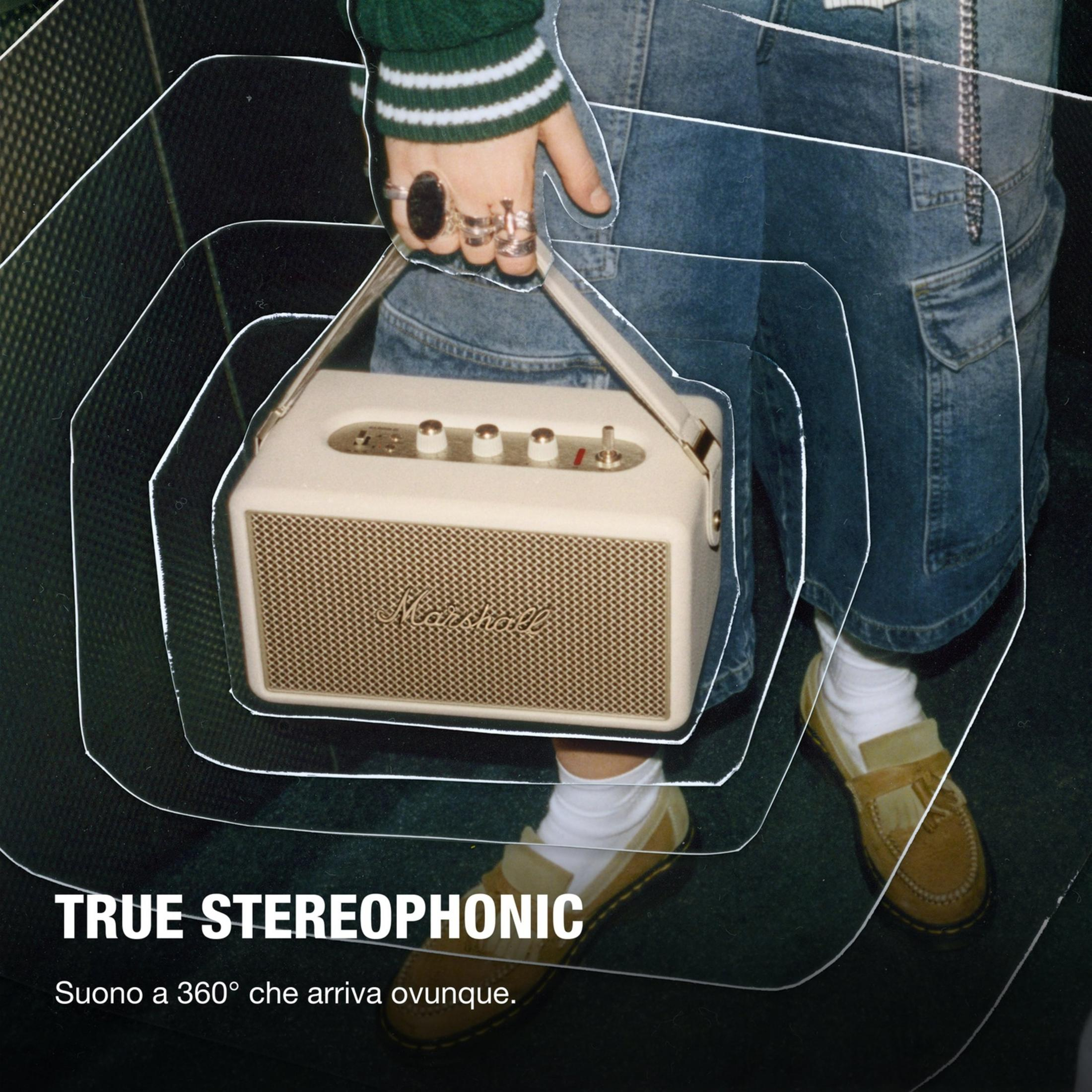 Una persona tiene una cassa Marshall. Indossa jeans e un maglione verde.