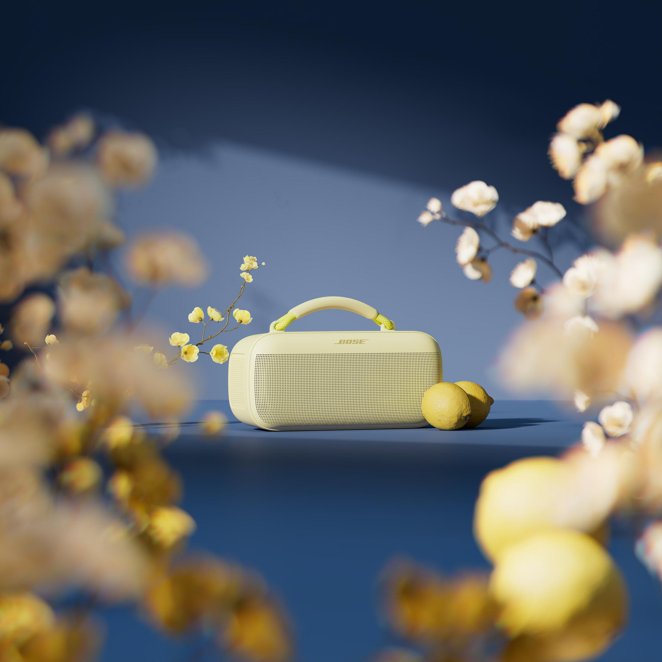 Jasnożółty głośnik Bose z uchwytem, dwa cytryny i kwitnące gałązki.