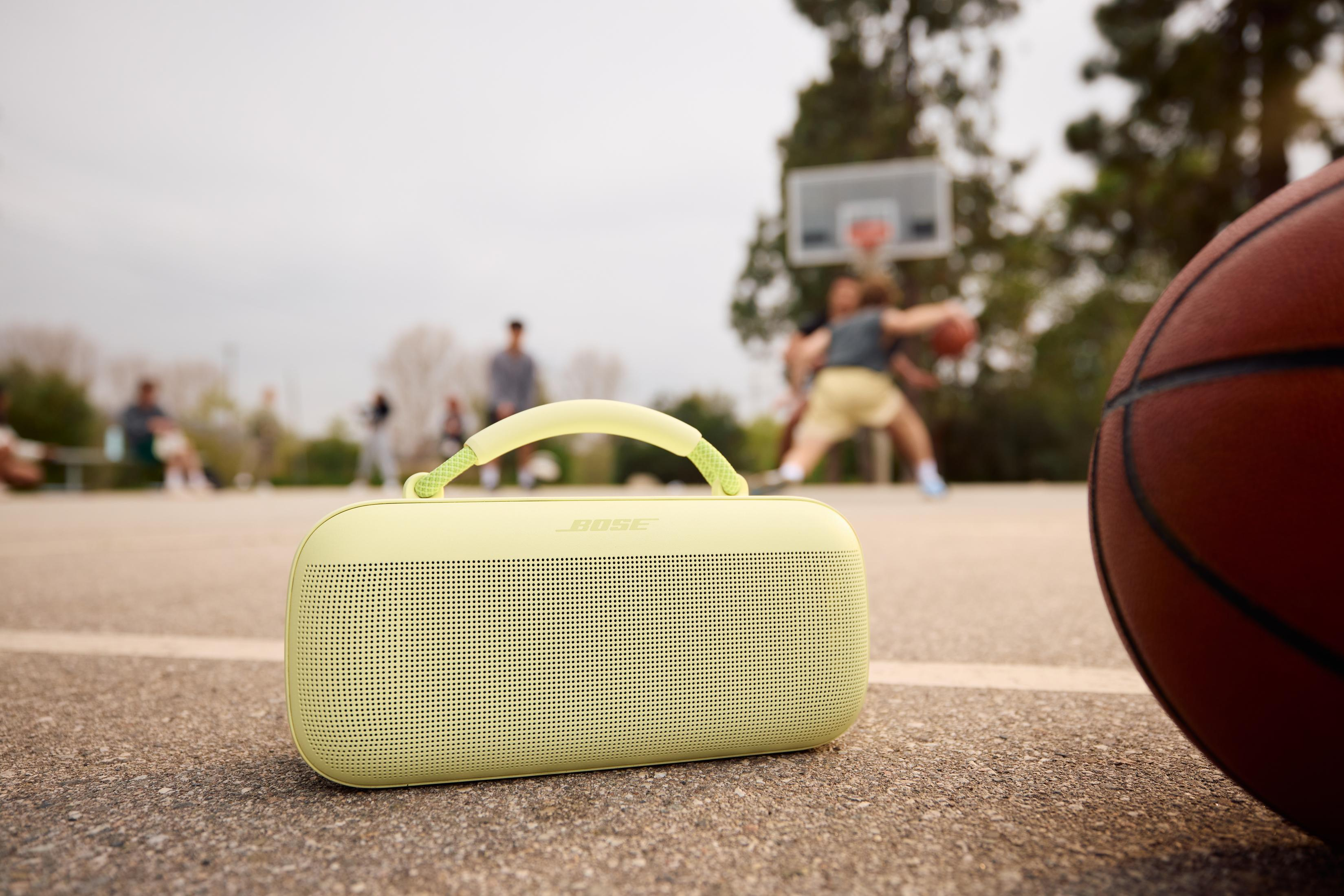 Jasnozielony głośnik Bose na boisku do koszykówki obok piłki.