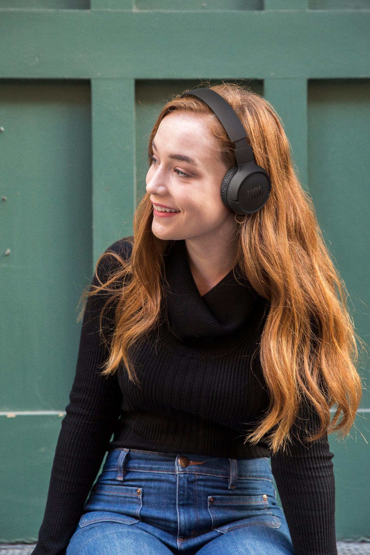 Młoda rudowłosa kobieta nosi słuchawki i czarną bluzkę.