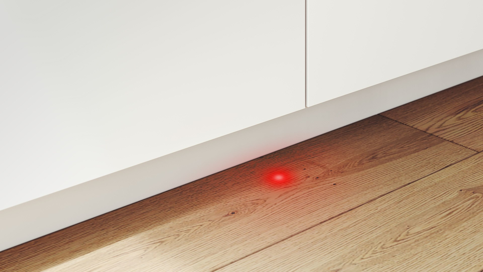 Czerwone światło świeci na drewnianej podłodze obok białej szafki.