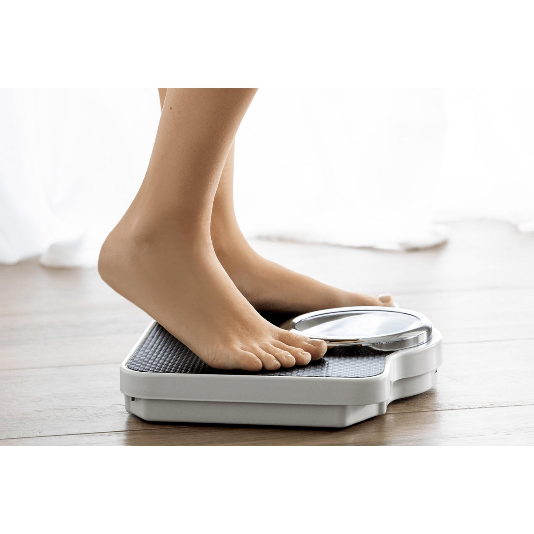 Stopy osoby na białej wadze na drewnianej podłodze.