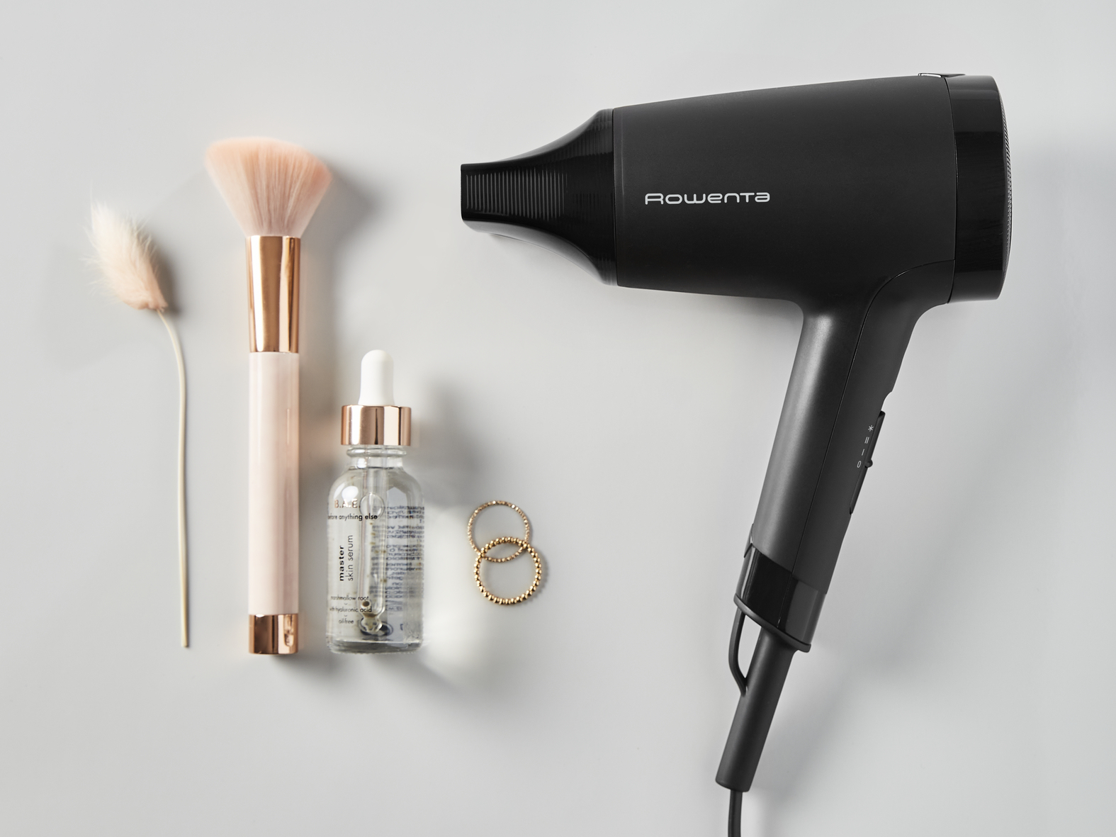 Czarna suszarka do włosów Rowenta z kosmetykami i biżuterią na szarym tle.