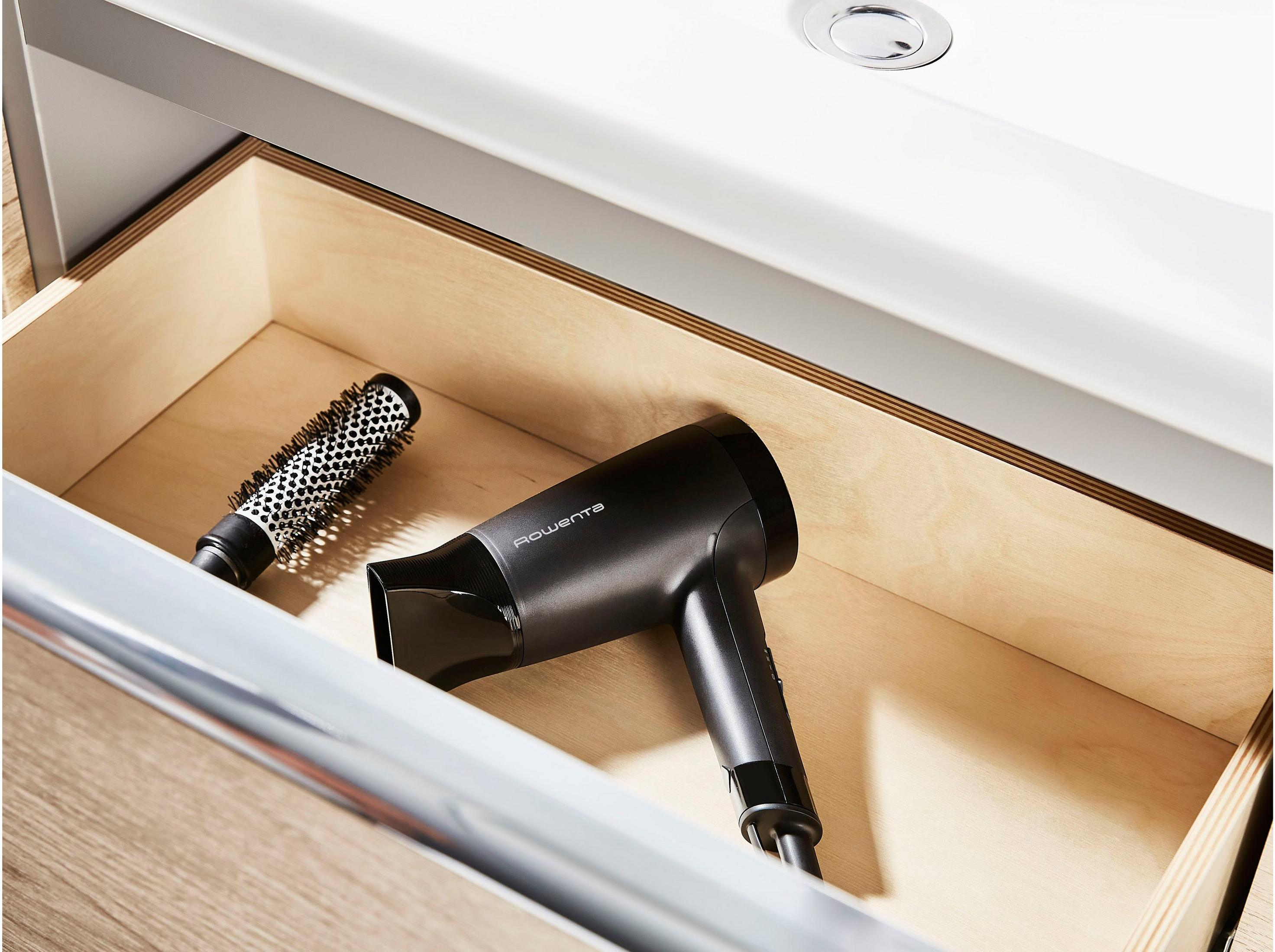 Czarna suszarka do włosów i szczotka leżą w otwartej drewnianej szufladzie.