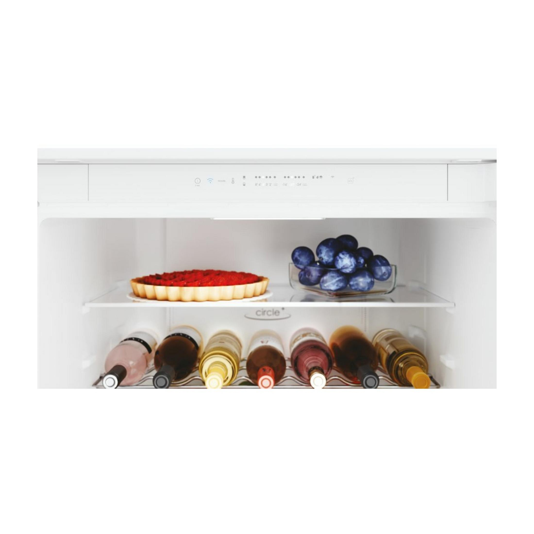 Tarta i niebieskie śliwki na półce, pod nimi butelki.