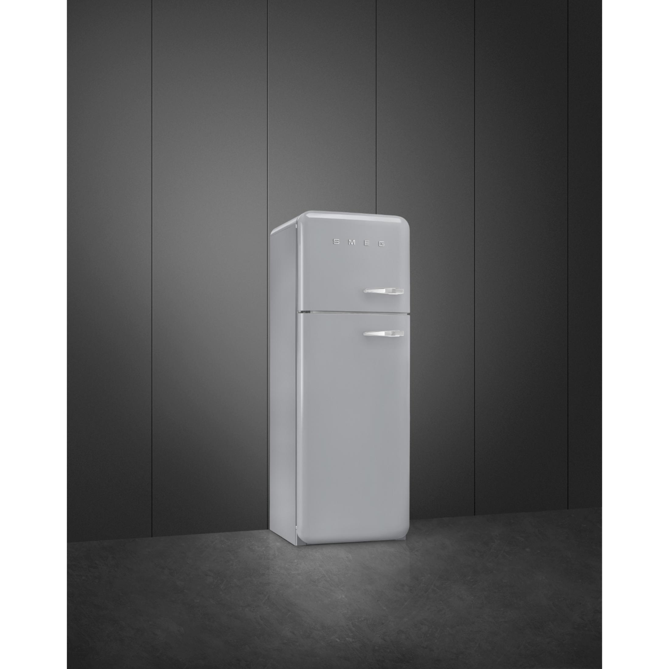 Un refrigerador SMEG gris de dos puertas se encuentra ante una pared oscura.