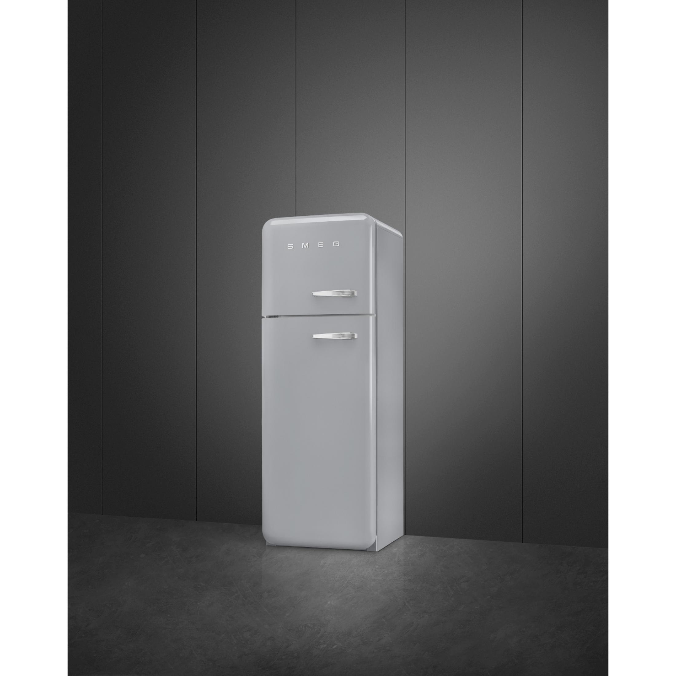 Un refrigerador SMEG gris con tiradores plateados se alza sobre un suelo oscuro ante una pared oscura.