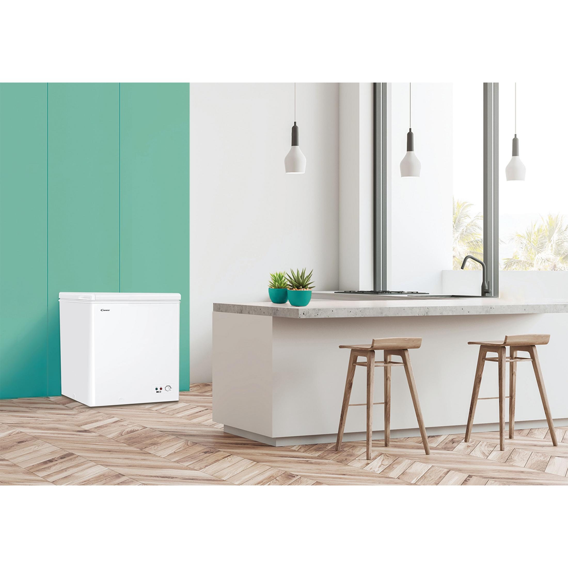 Un congelador horizontal blanco sobre suelo de madera junto a isla de cocina con taburetes.