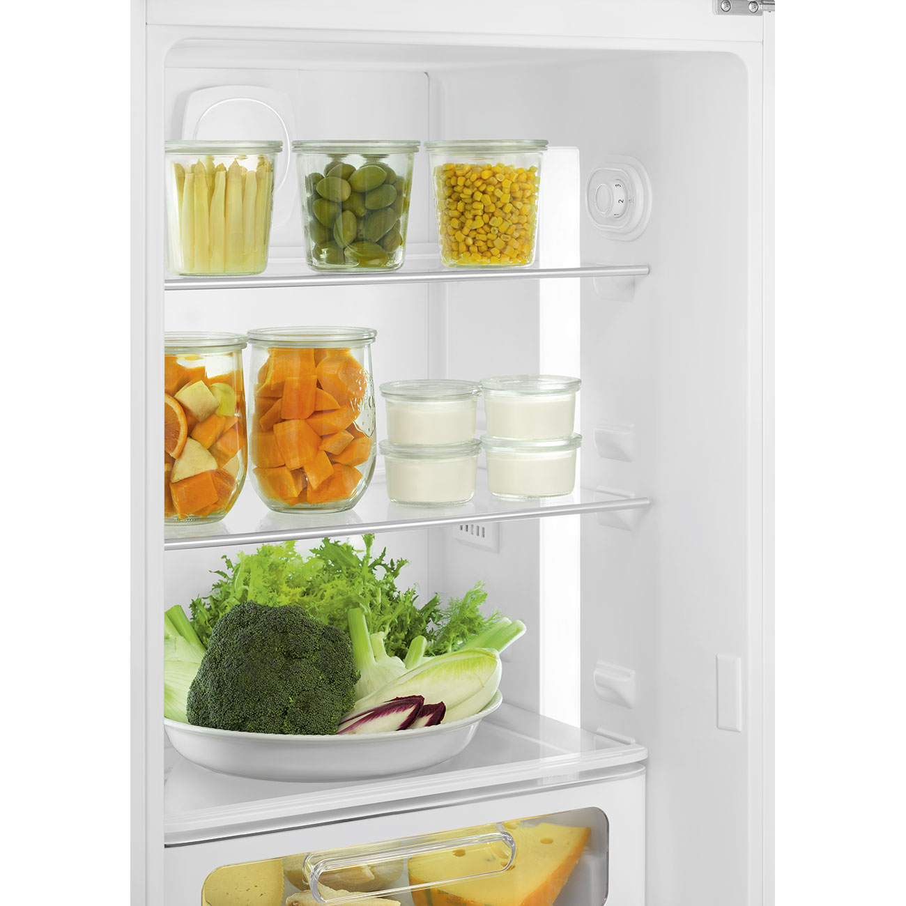 Estantes de refrigerador con frascos de espárragos, aceitunas, maíz, naranjas, zanahorias, yogur, ensalada y queso.