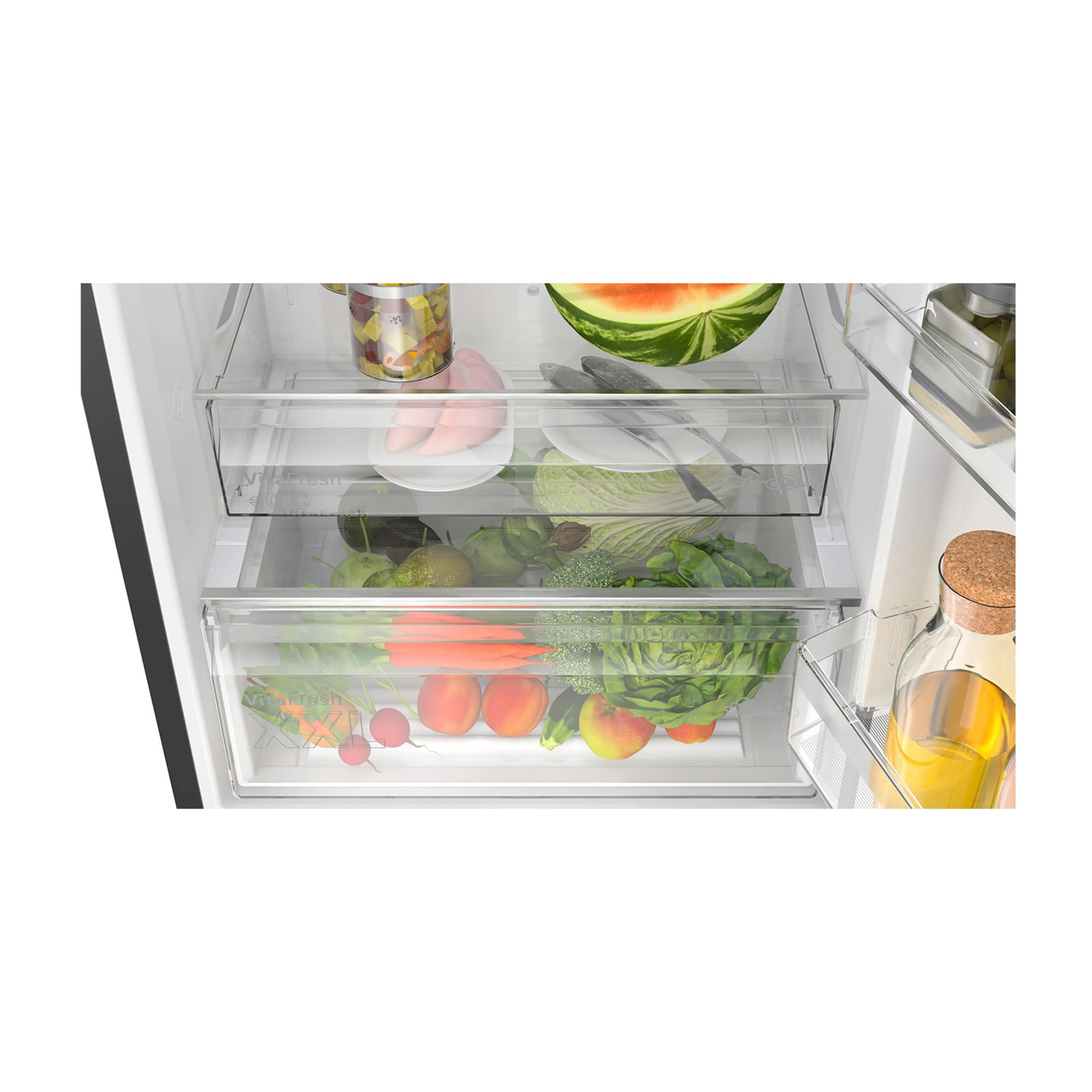 Offener Kühlschrank mit frischem Obst und Gemüse in Schubladen. Wassermelonenscheibe sichtbar.