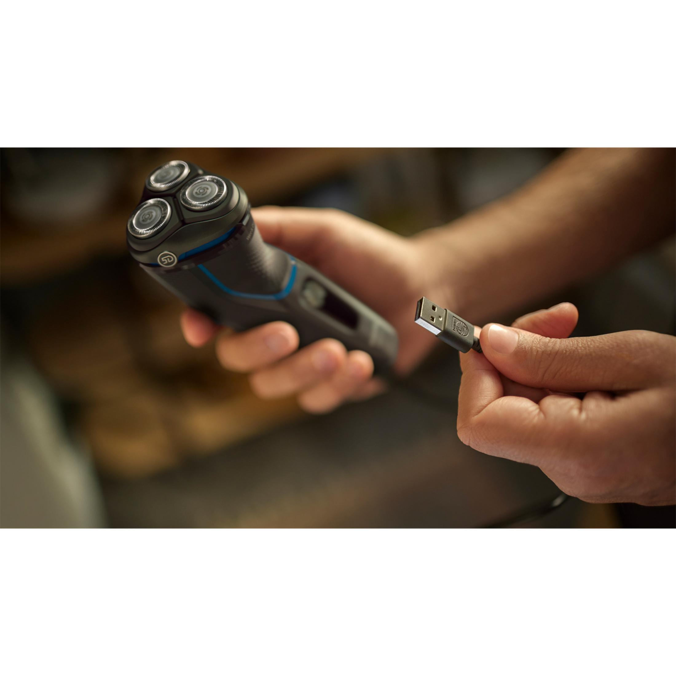 Osoba trzyma czarną golarkę i kabel USB.