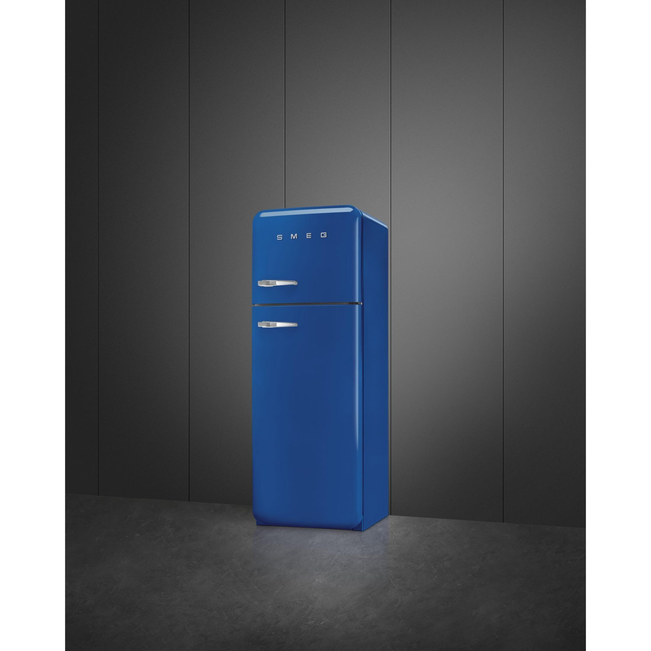 Un refrigerador azul de dos puertas con tiradores plateados se alza sobre suelo oscuro.