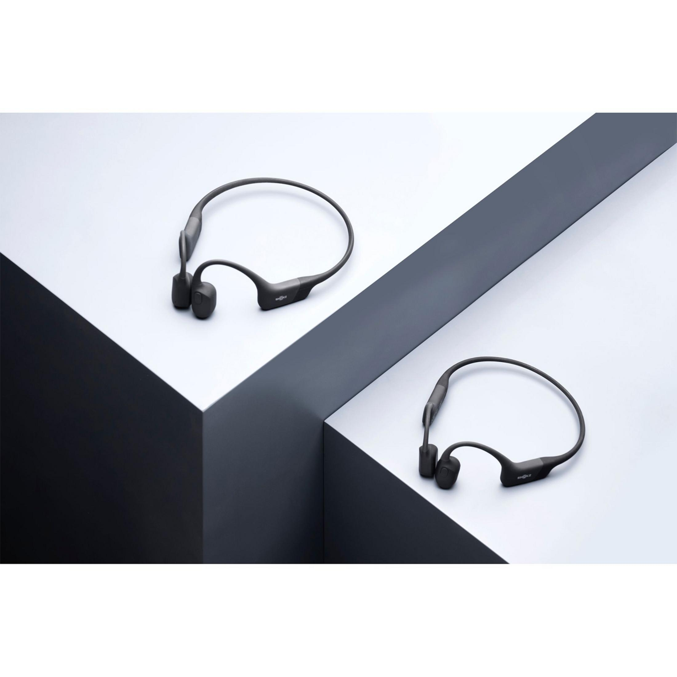 Dwa ciemne słuchawki spoczywają na białych i szarych powierzchniach.
