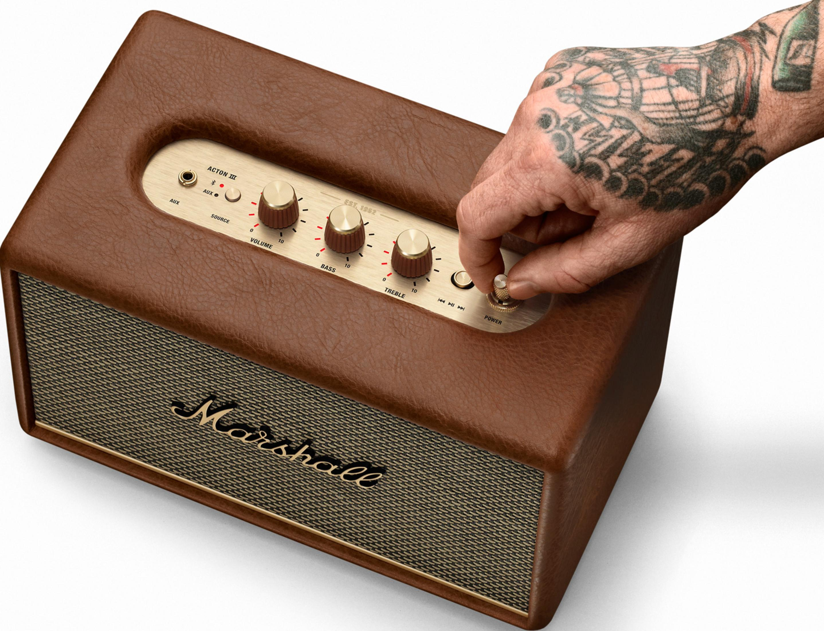 Una mano tatuada gira el mando de encendido de un amplificador Marshall marrón.