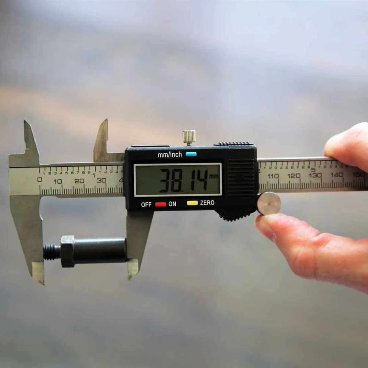 Ein digitales Messschieber misst ein schwarzes Bauteil. Anzeige: 38.14 mm.