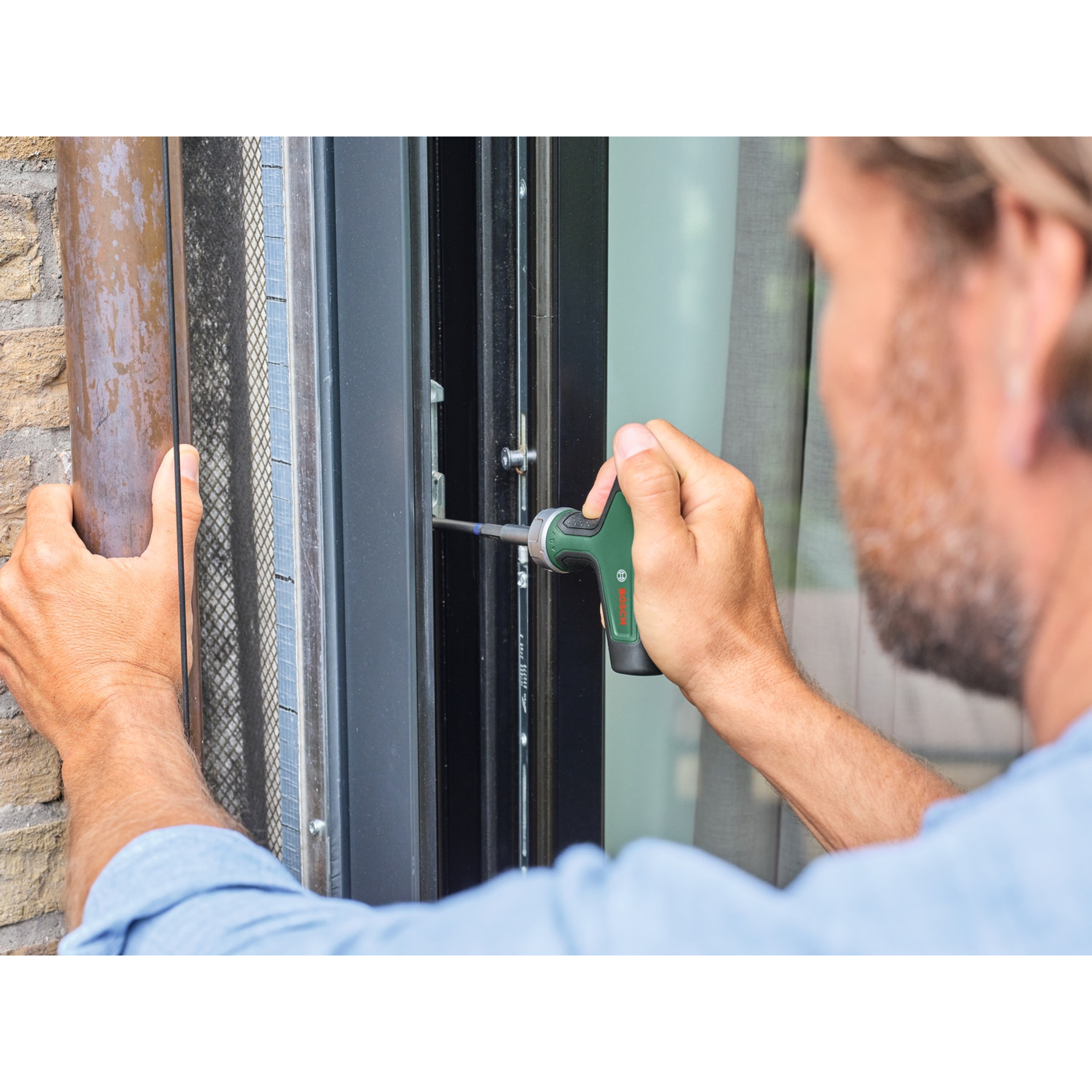 Mann repariert Fenster mit Schraubendreher. Fokus auf Hände und Werkzeug.