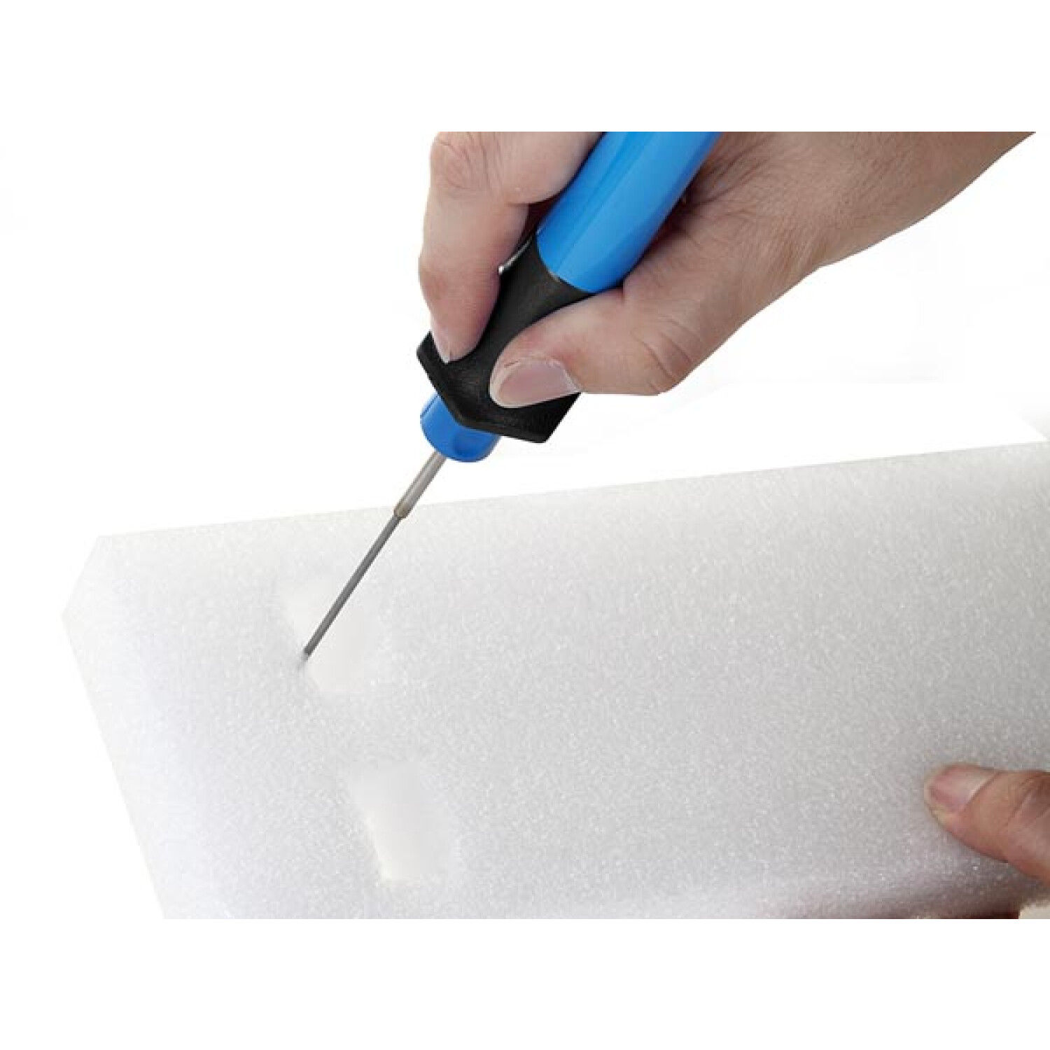 Eine Hand hält ein blaues Werkzeug und schneidet in weißen Schaumstoff.