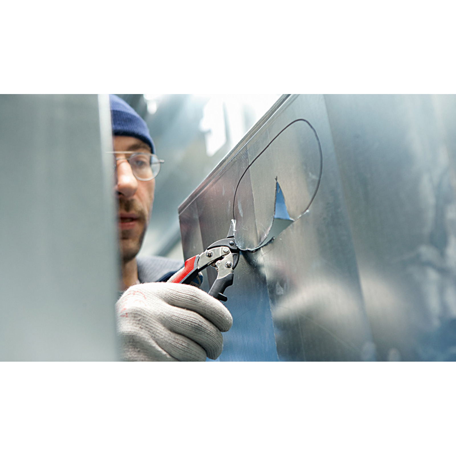 Mann mit blauer Mütze schneidet Metall mit Schere.