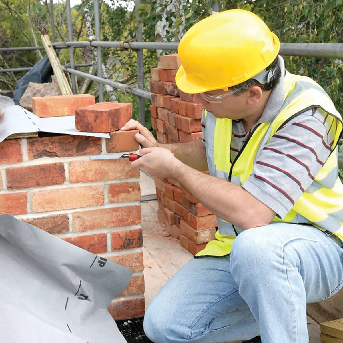 Ein Maurer in gelbem Helm baut eine Ziegelwand auf einer Baustelle.