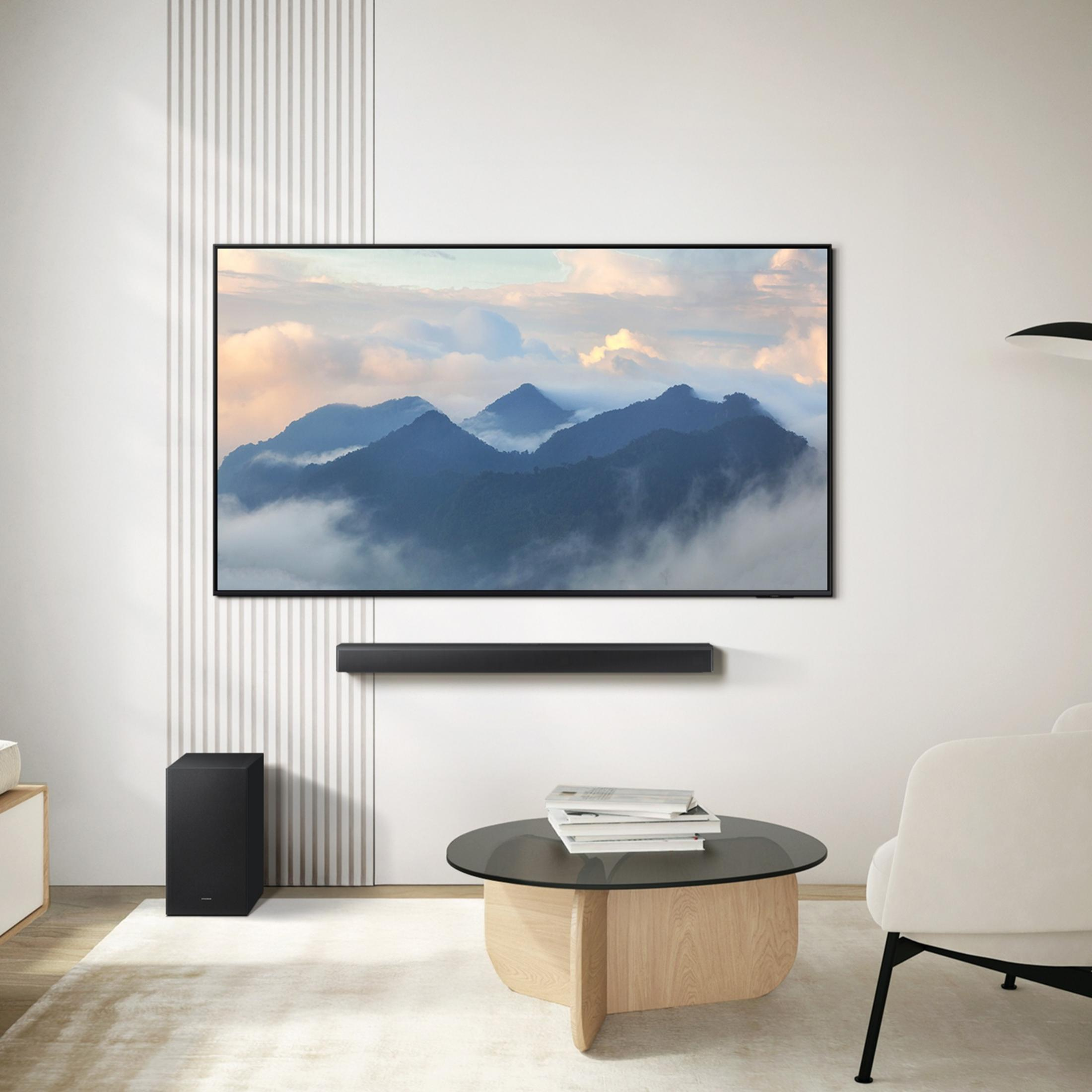 Salon moderne avec grande TV affichant des montagnes, subwoofer et table basse.