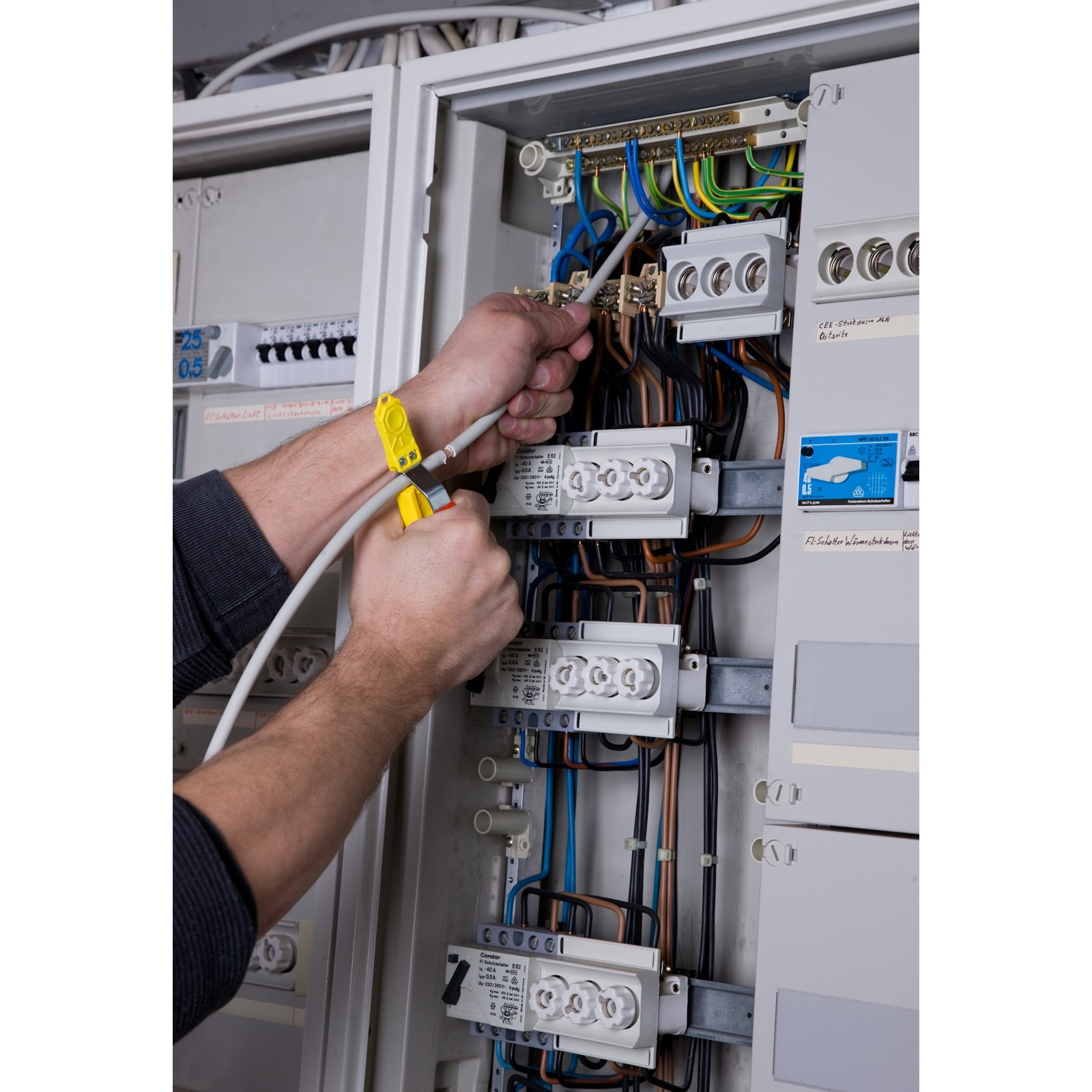 Elektriker arbeitet an Sicherungskasten mit Kabeln und Sicherungen.