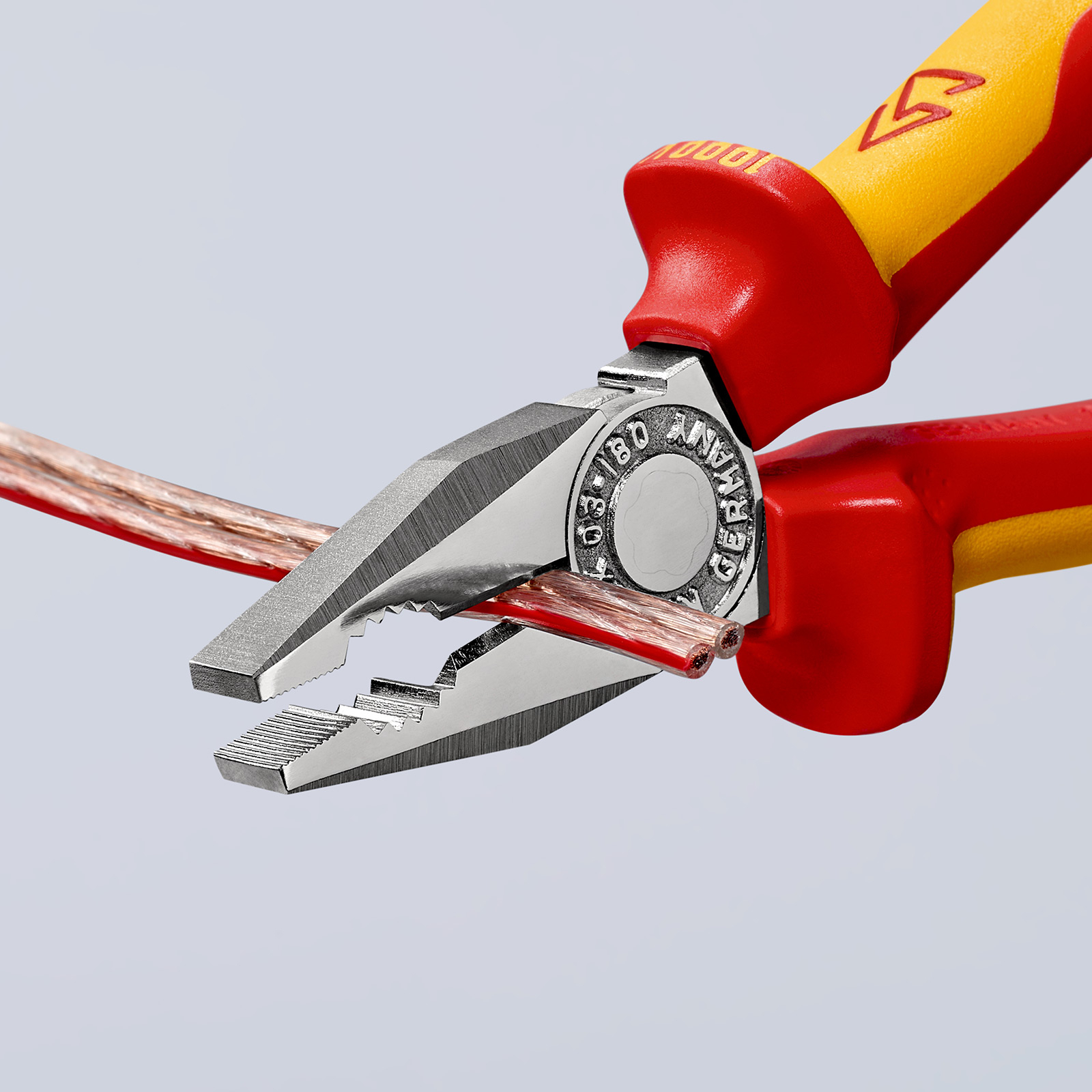 Eine rote und gelbe Zange hält ein Kabel mit Kupferdraht. Detailaufnahme.
