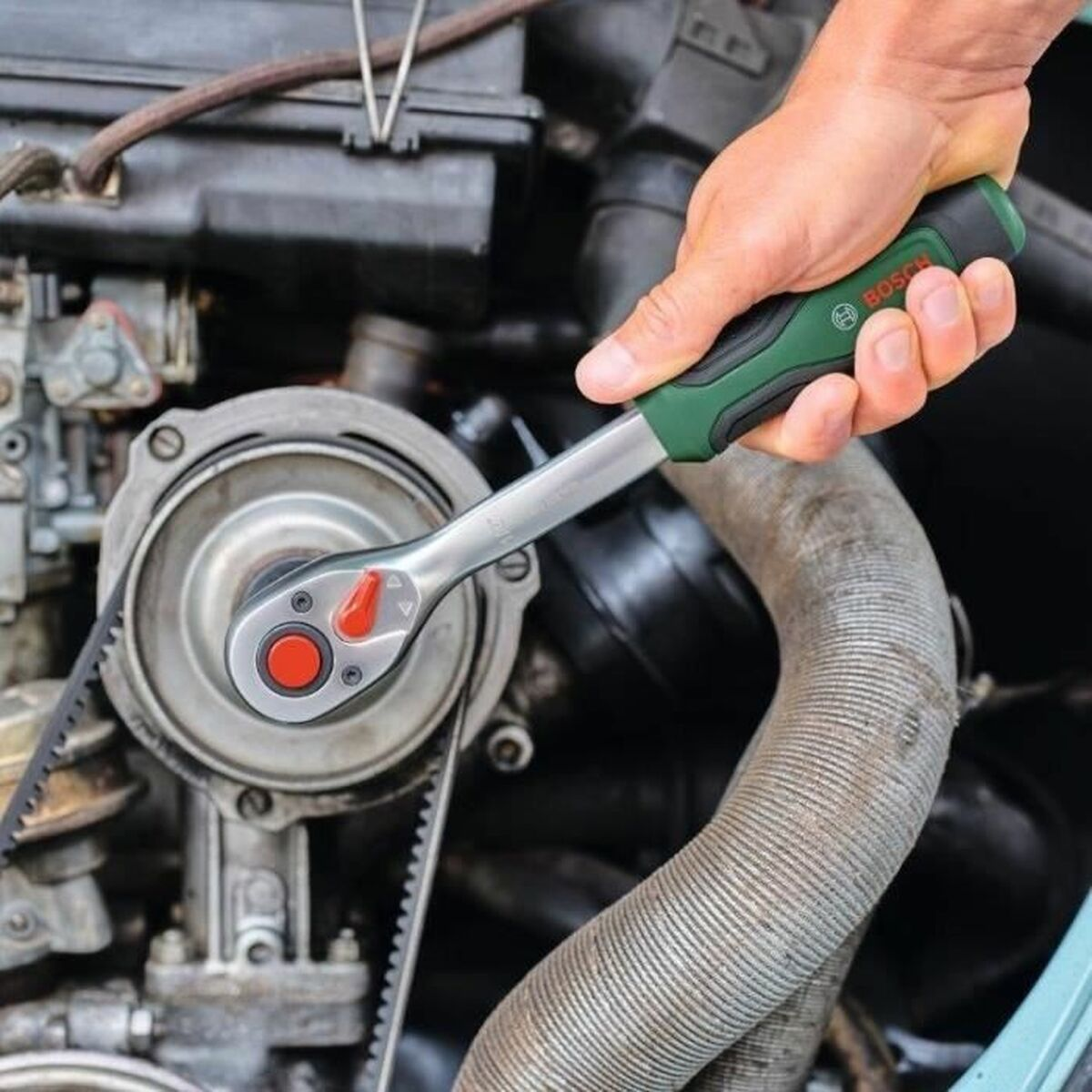 Eine Hand benutzt einen Bosch-Ratschenschlüssel an einem Motor. Ein Riemen ist sichtbar.