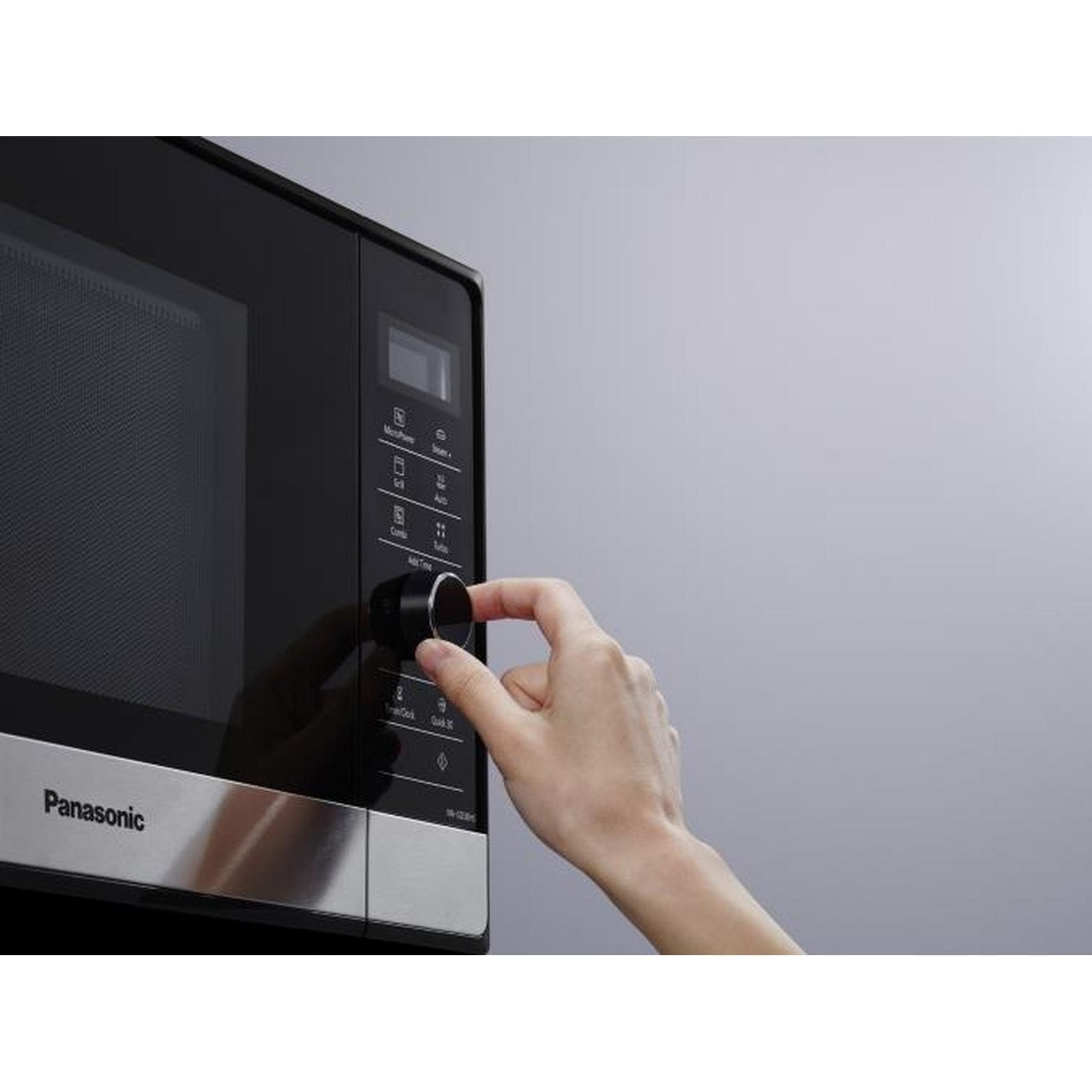 Ręka obraca pokrętło na czarnej kuchence mikrofalowej Panasonic z srebrnym wykończeniem. Ekran widoczny.