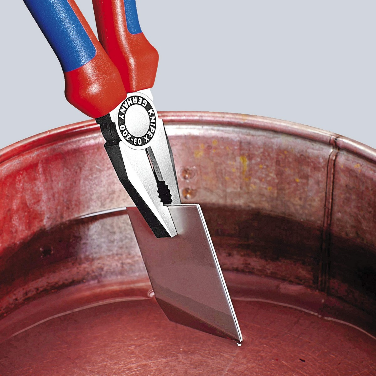 Eine Zange mit rot-blauen Griffen hält ein Metallstück in einer roten Schale.