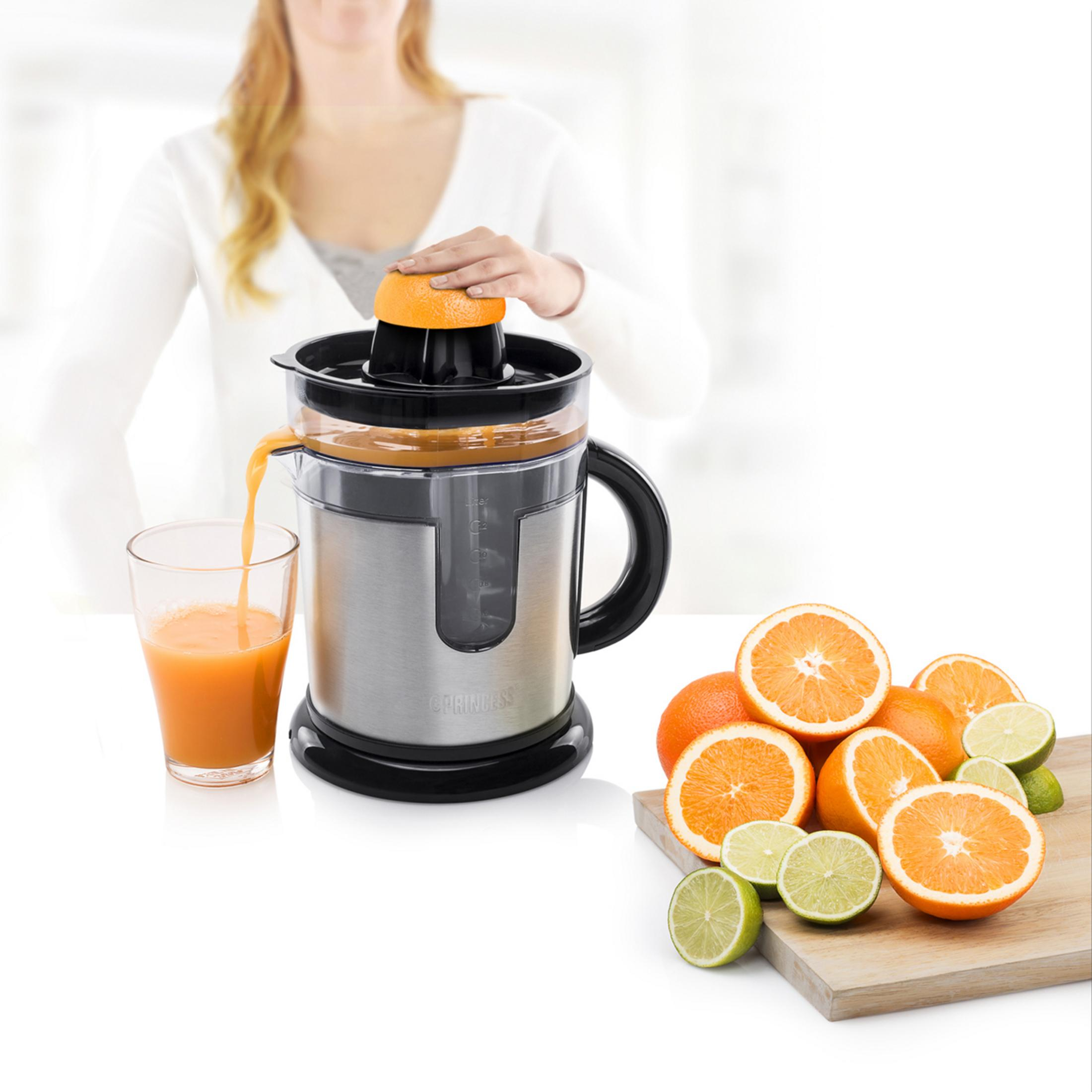 Eine Frau presst eine Orange in einem Entsafter aus. Saft fließt in ein Glas.