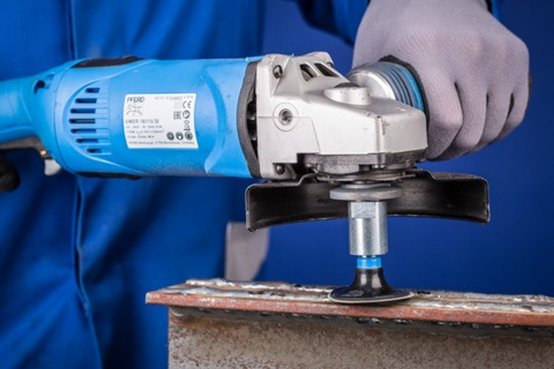 Ein Handwerker schleift Metall mit einem Winkelschleifer und blauer Kleidung.