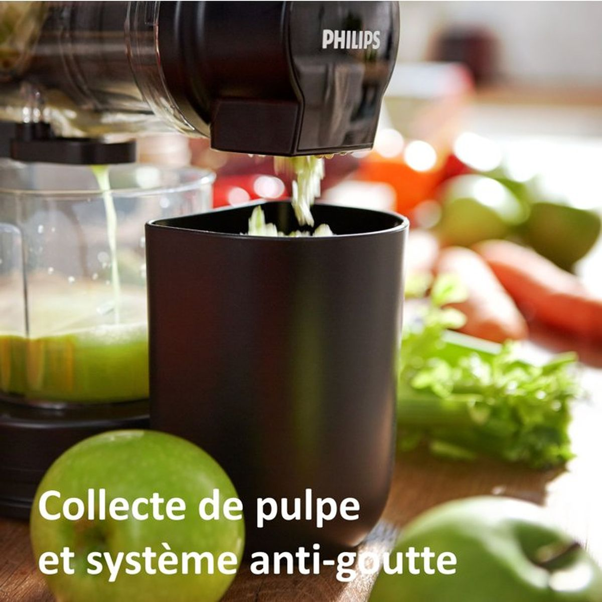 Ein Philips-Entsafter verarbeitet Obst und Gemüse zu Saft. Grüne Äpfel und Karotten im Hintergrund.