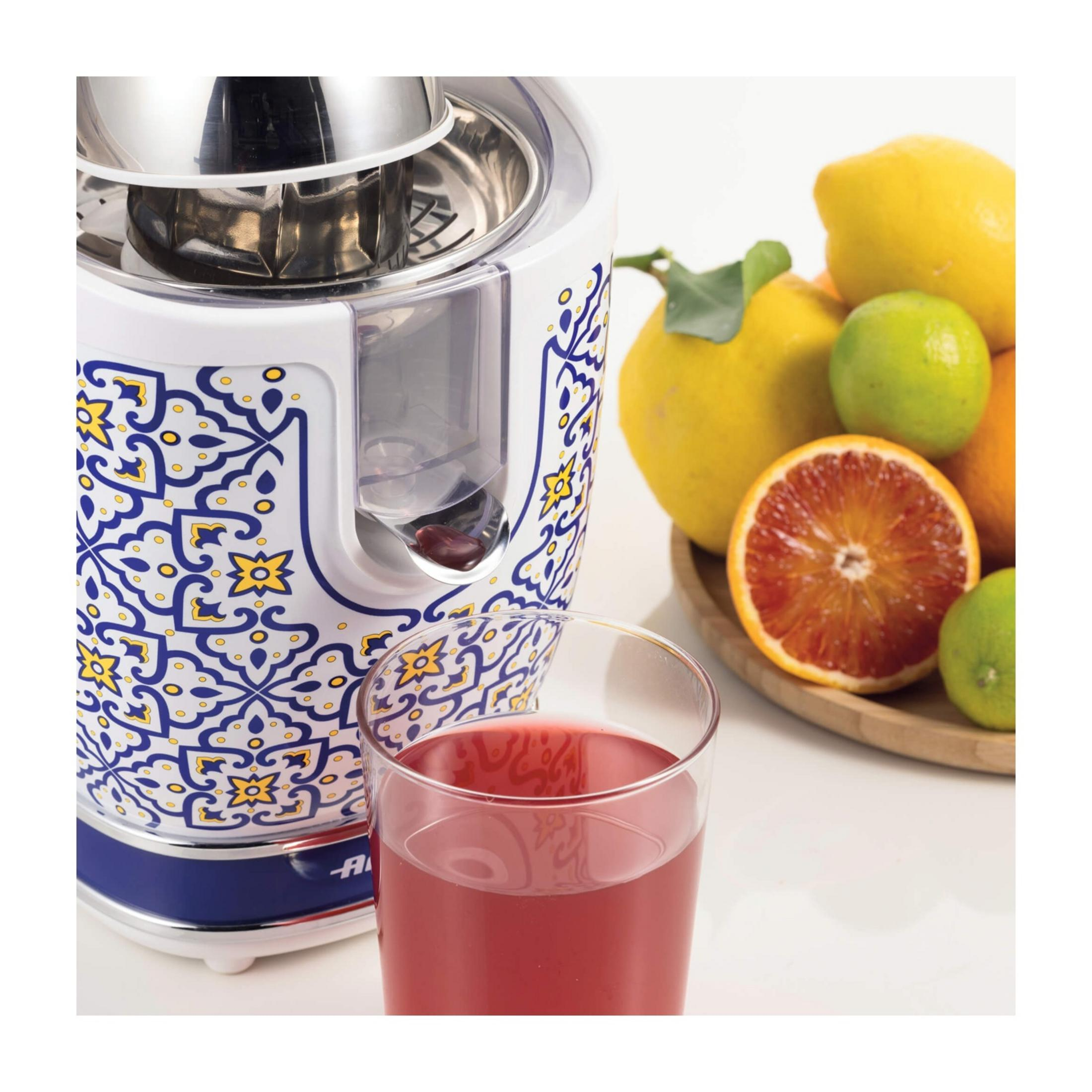Sokowirówka z niebiesko-żółtym wzorem stoi obok szklanki soku i świeżych cytrusów.