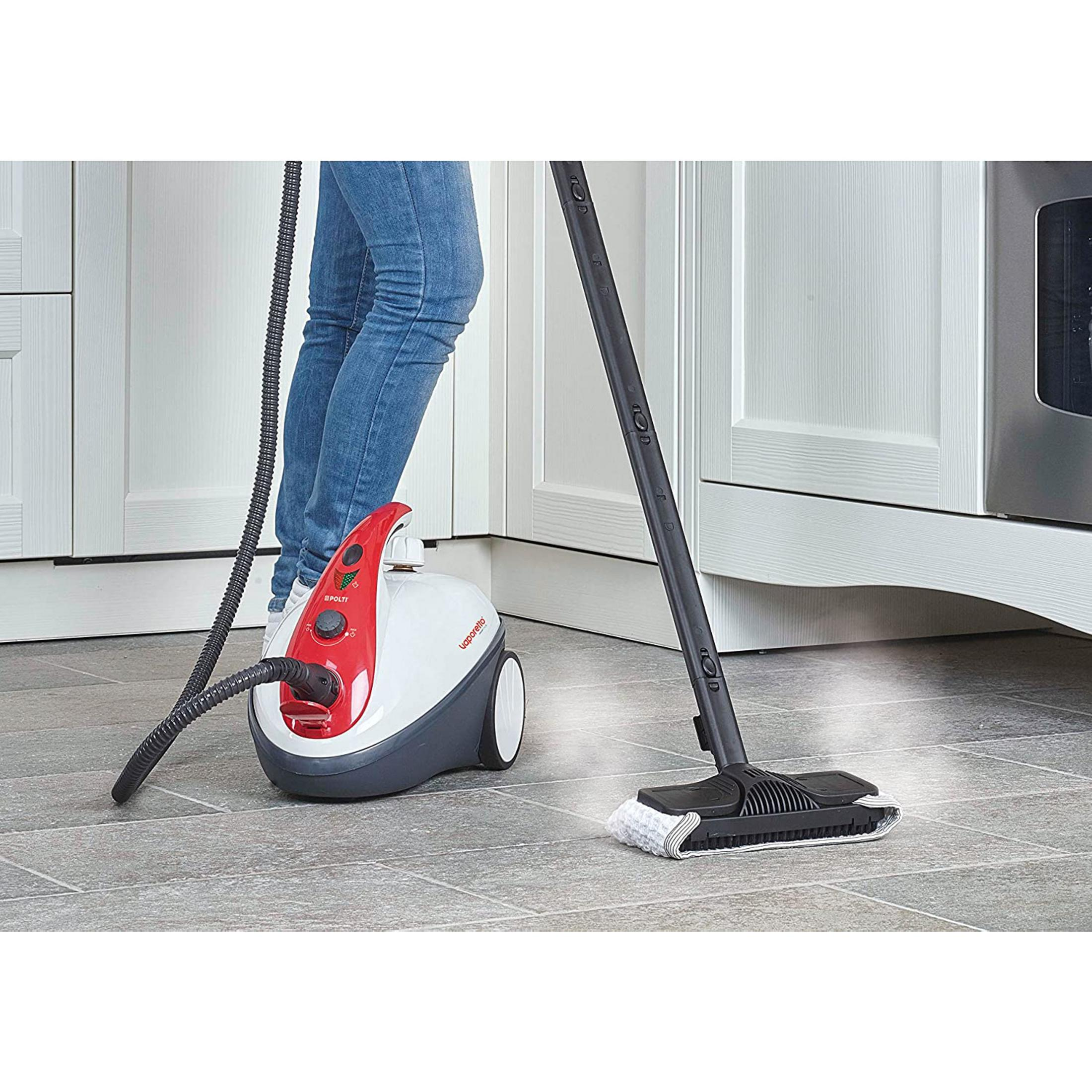 Osoba czyści podłogę parownicą. Białe szafki w tle.